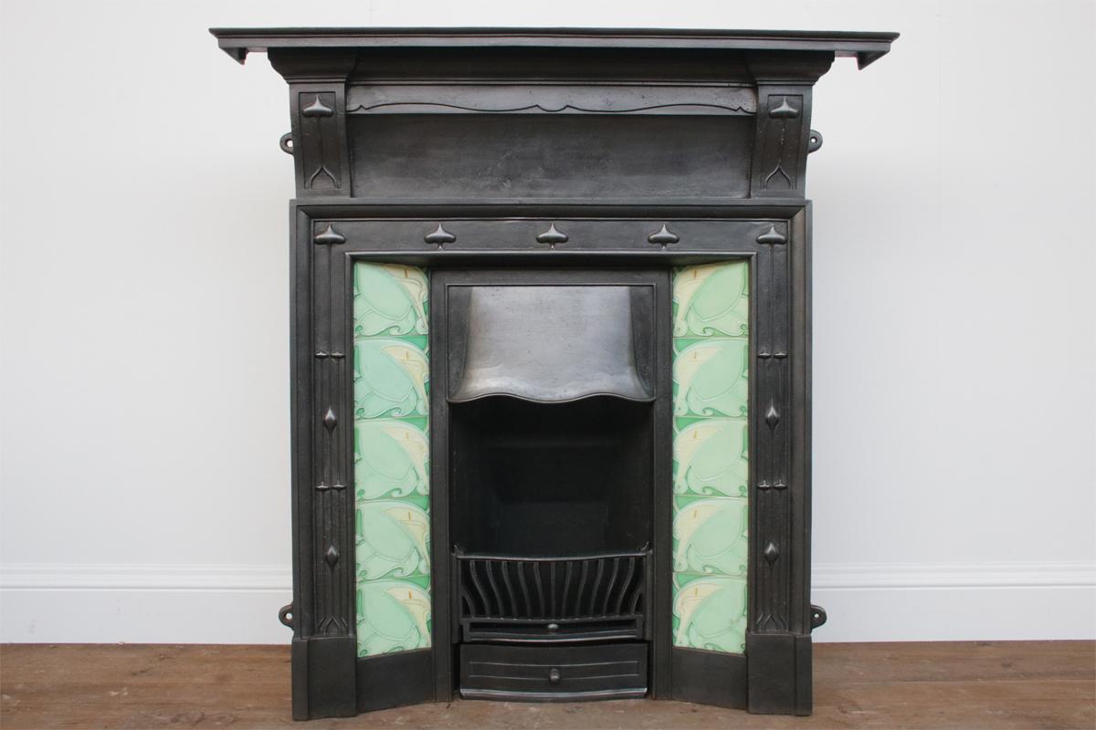 Large antique Edwardian cast iron combination fireplace with a simple surround, but finely cast ornate canopy, circa 1900. Complete with an original set of bookmatched fireplaces tiles depicting stylised Arum Lillies.

This grate has been finished