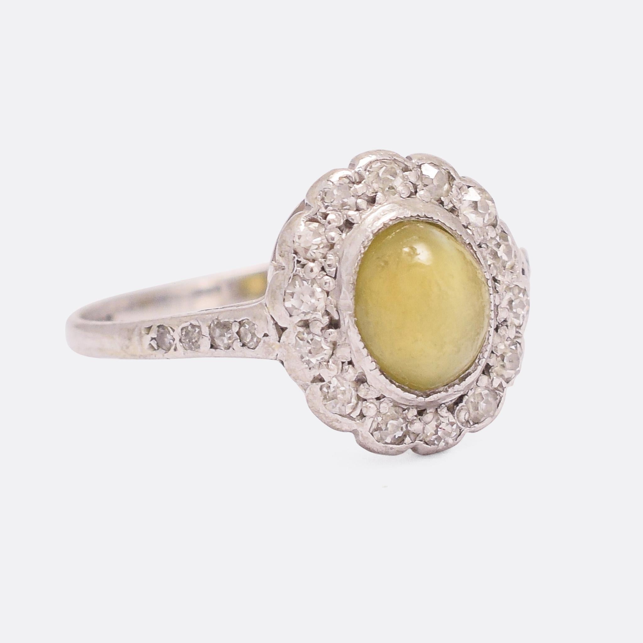 A charming antique cat's eye flower ring dating from the Edwardian era, circa 1910. The principal stone rests in a millegrain bezel setting, surrounded by a halo of white diamonds - each one set into a petal-like mount. The band is worked in 18k