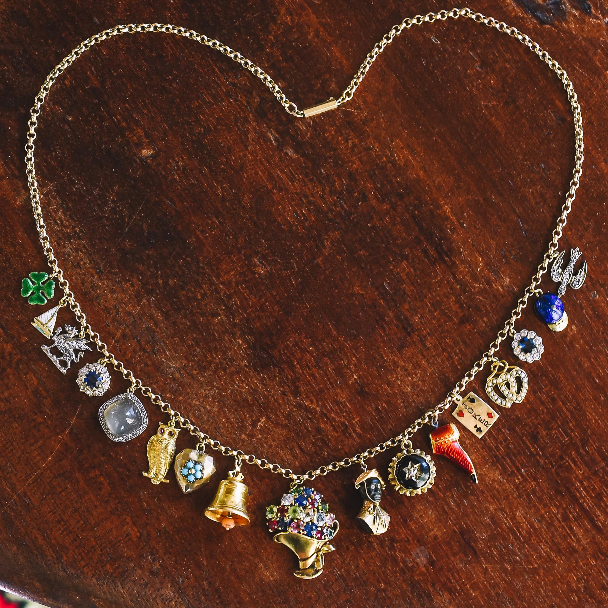 An outstanding antique charm necklace featuring a collection put together in the first few decades of the 20th century (based on dates engraved on some of the charms). Highlights include: owl with garnet eyes; multigem giardinetti; two sapphire and