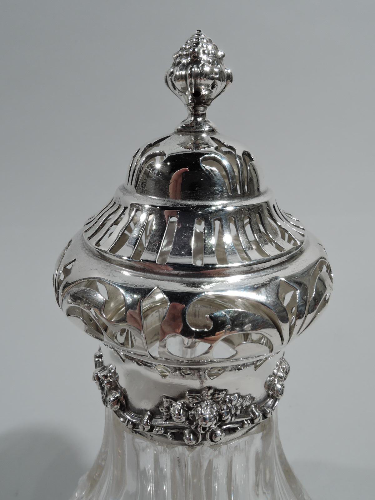 Turn-of-the-century American Edwardian Classical sterling silver and crystal sugar shaker. Each: Fluted glass baluster body with sterling silver mounts: plain collar and raised foot with flutes and scrolls. Cover double-domed and pierced with berry