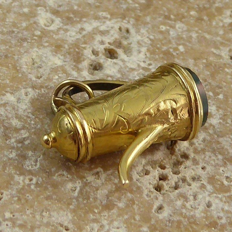 An antique fob style gold charm dating from the late Edwardian era.  In the form of a coffee pot, the charm is very nicely detailed with a floral hand engraved pattern to the body and cover of the coffee pot. The base is a flat disc of bloodstone