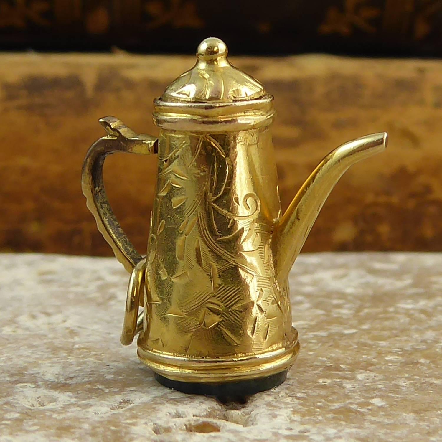 An antique fob style gold charm dating from the late Edwardian era.  In the form of a coffee pot, the charm is very nicely detailed with a floral hand engraved pattern to the body and cover of the coffee pot. The base is a flat disc of bloodstone