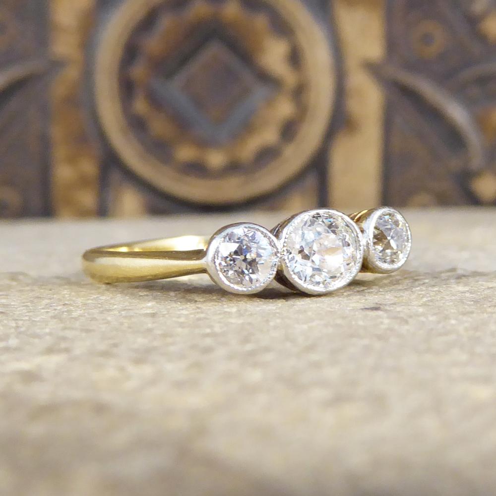 This beautiful three stone ring was hand crafted in the Edwardian era from 18ct Yellow Gold and Platinum. The three Old Cut Diamonds are set in a rub over collar setting with a millegrain detail in Platinum, leading down to a Yellow Gold band. Such