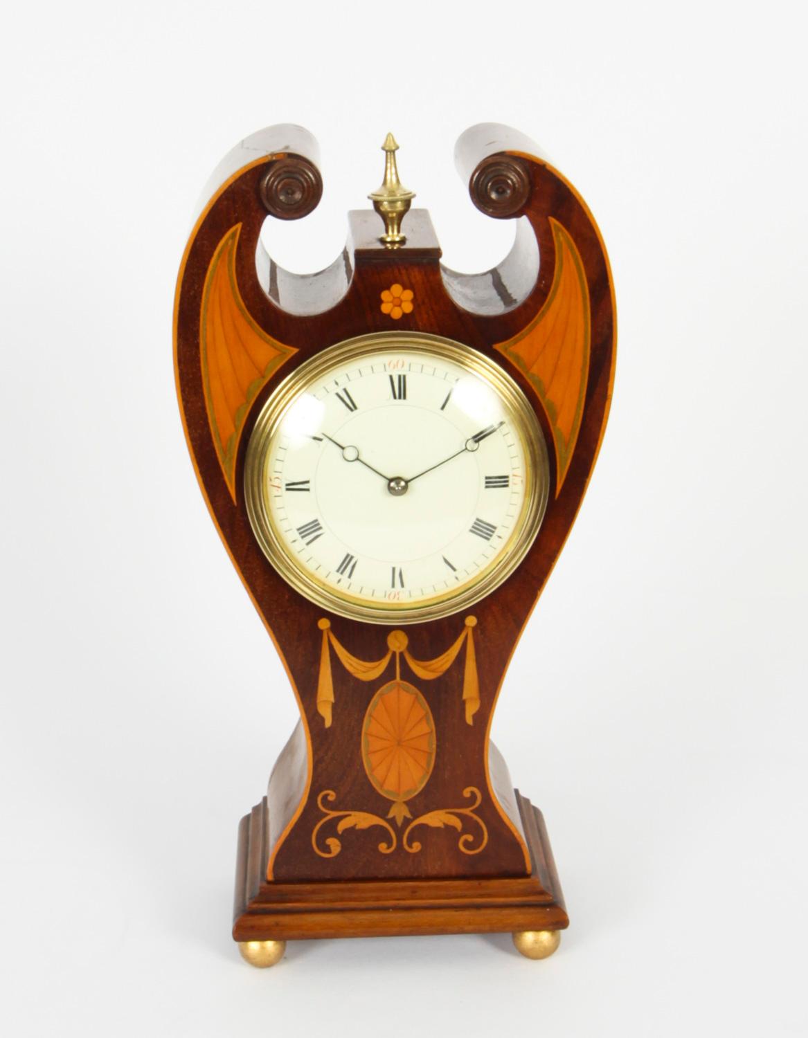 This is a pretty antique Edwardian inlaid mahogany mantel clock, circa 1900 in date,  complete with the original winding key.

It has a beautiful beautiful shaped case with string inlay, ribbon and garland and  conch shell detail, with enamelled