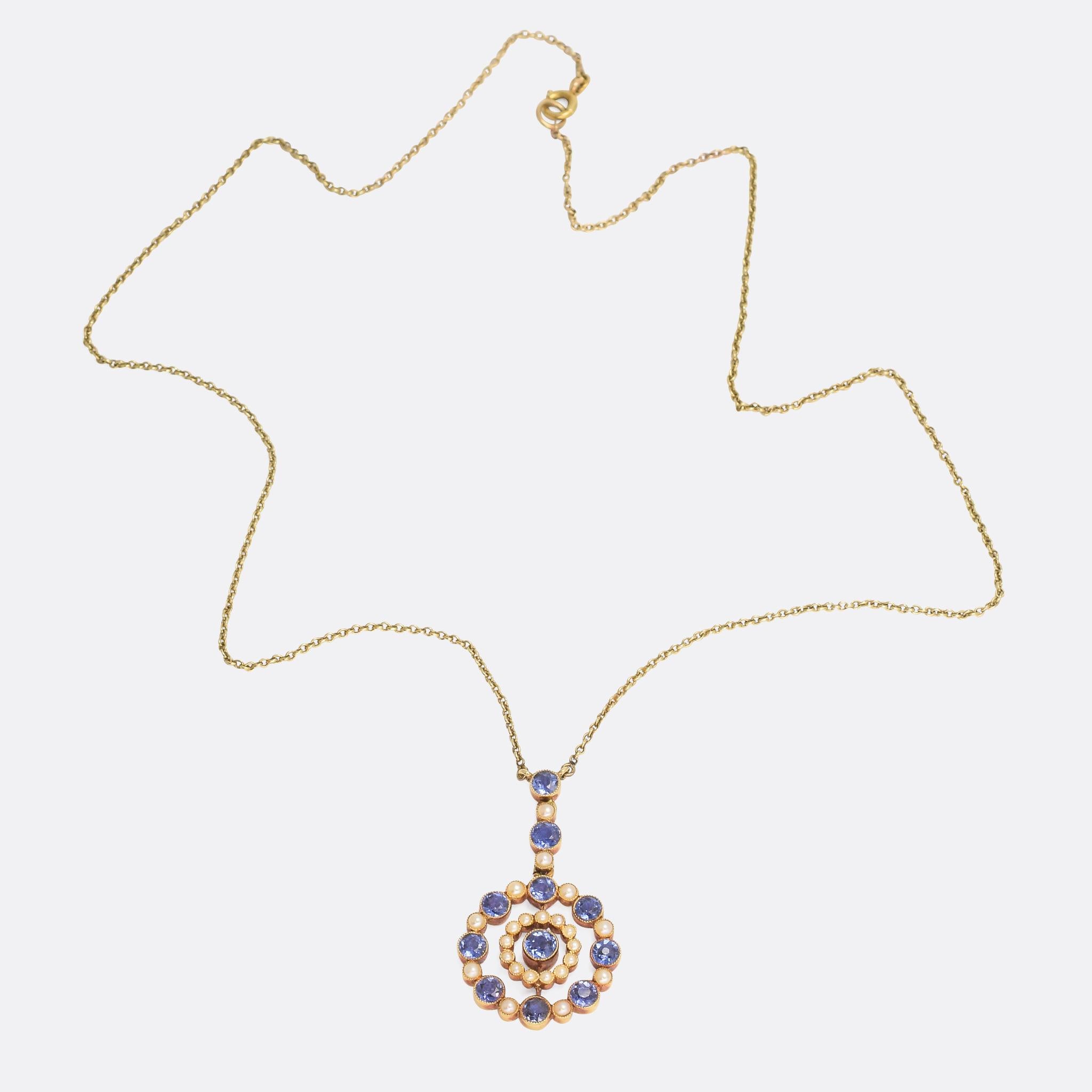 An exquisite antique necklace; the pendant is set with cornflower blue sapphires and natural pearls to form a double halo / target motif around the central stone. It's modelled in 15 karat yellow gold, with millegrain collet settings - all crafted