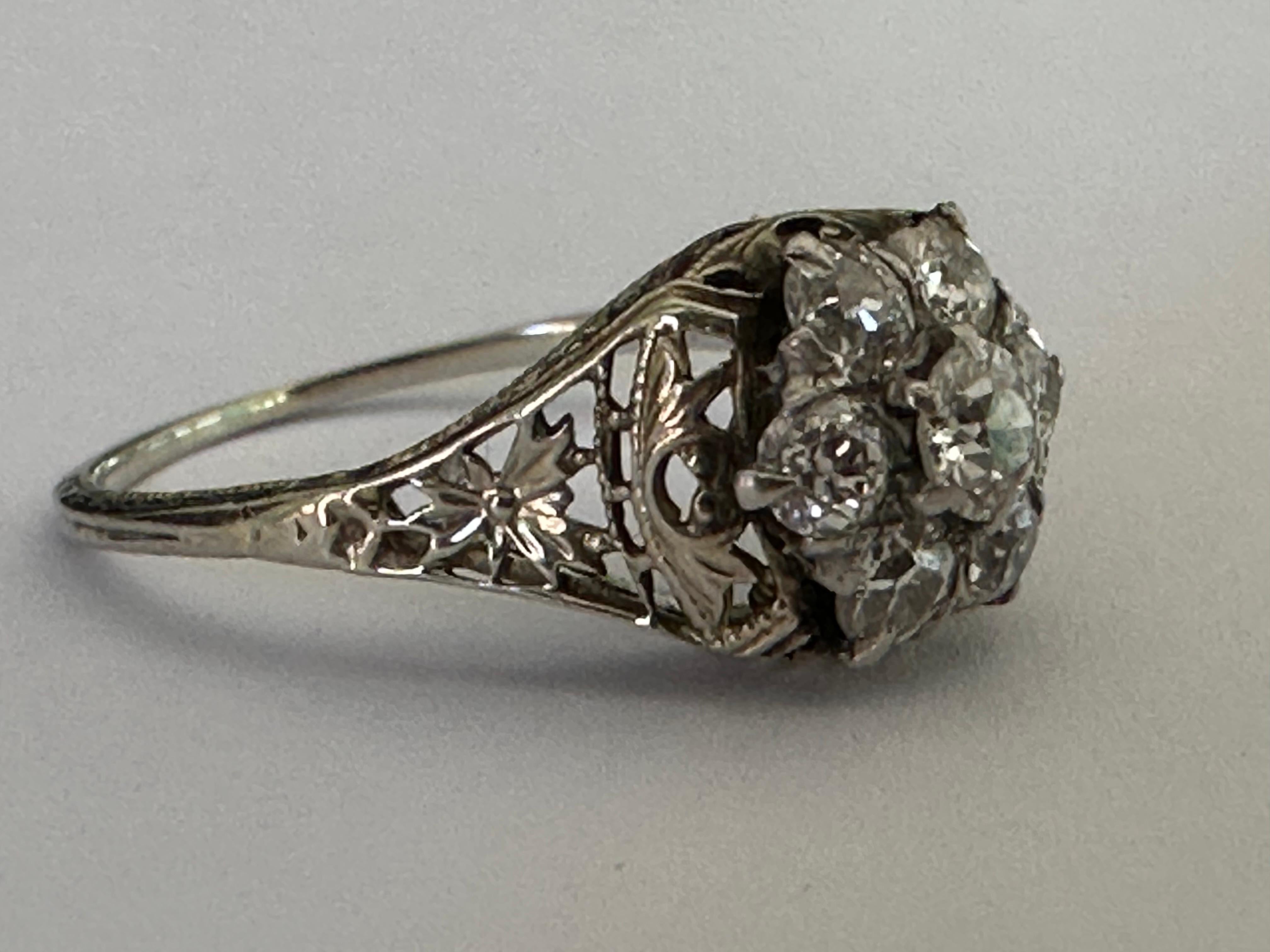 Crafted in the early 1900s, this Edwardian Era gem features seven Old European cut diamonds in a floral design weighing approximately 0.70 carats, G-H color, VS2 clarity, and set in an intricate filigree band fashioned in 18K white gold. 