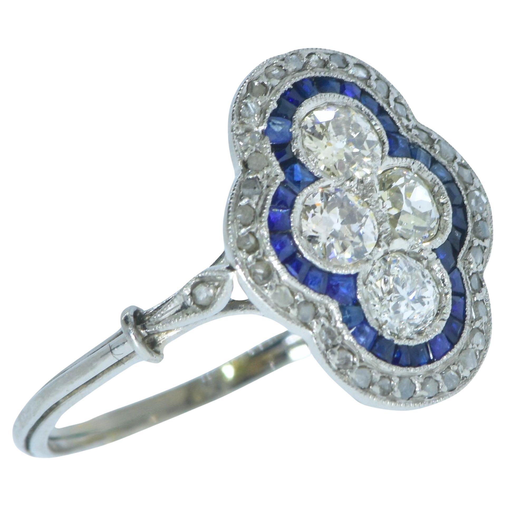 Bague ancienne édouardienne en platine ornée de diamants et de saphirs bleus vifs de taille fantaisie, à motif quadrilobé, vers 1915. Les quatre diamants centraux sont entourés de saphirs bleus vifs naturels taillés en calibre, qui sont ensuite