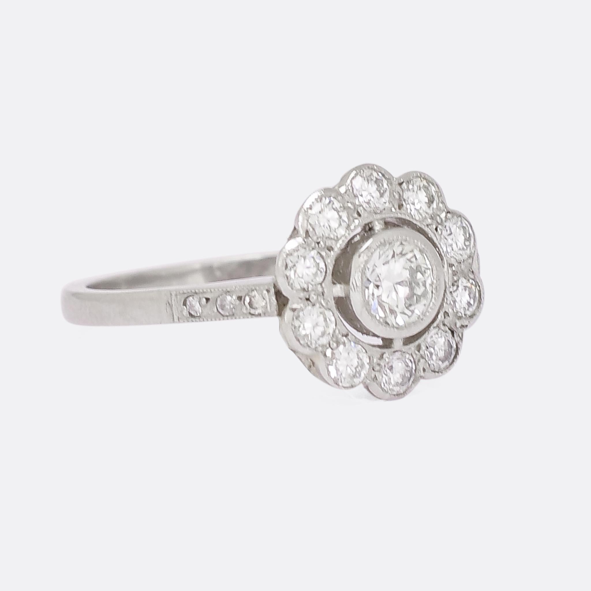 This stunning diamond cluster ring was made in the Edwardian era, circa 1910. The bright brilliant cut diamonds, .85ct total, are set in millegrain bezel settings with diamond shoulder accents, and the ring is modelled in platinum throughout. The
