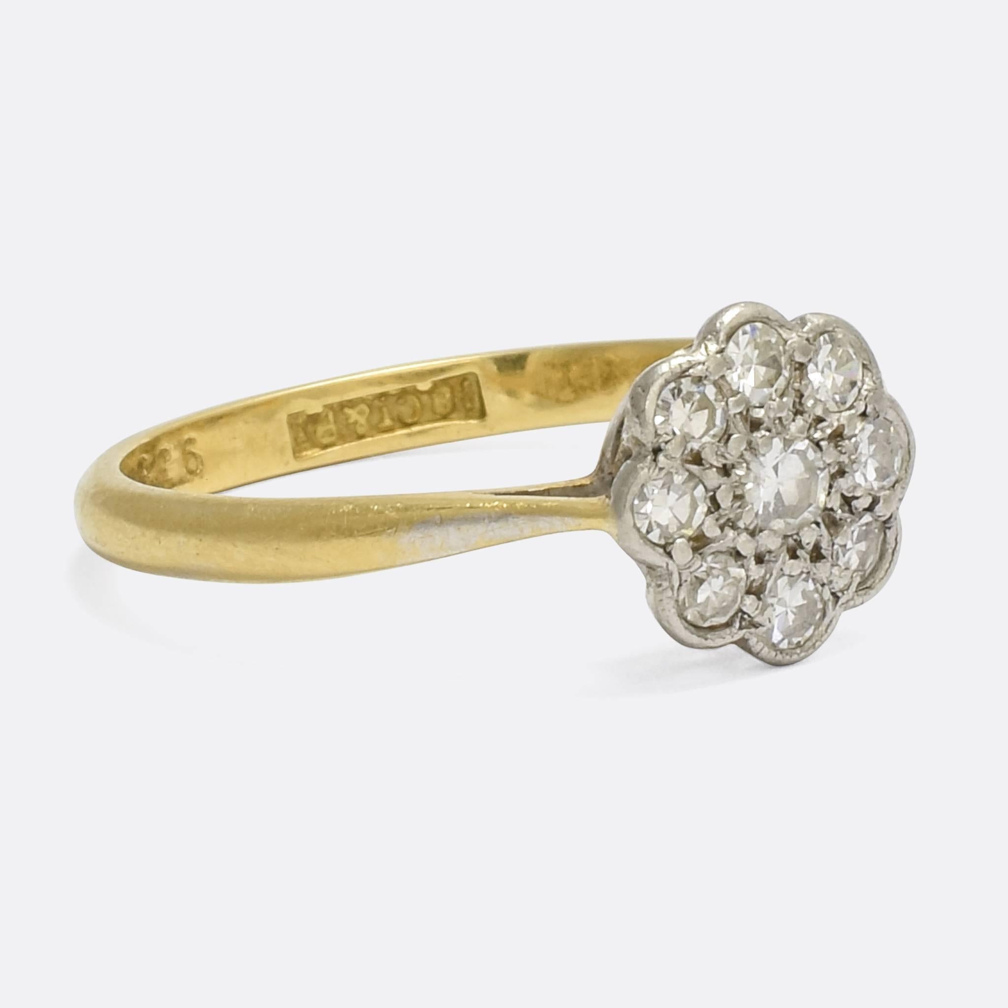 A pretty antique diamond cluster ring, the head modelled as a daisy. It dates to the early 20th Century, modelled in platinum and 18k yellow gold with a pierced gallery that allows light in behind the stones. The platinum settings are finished in a