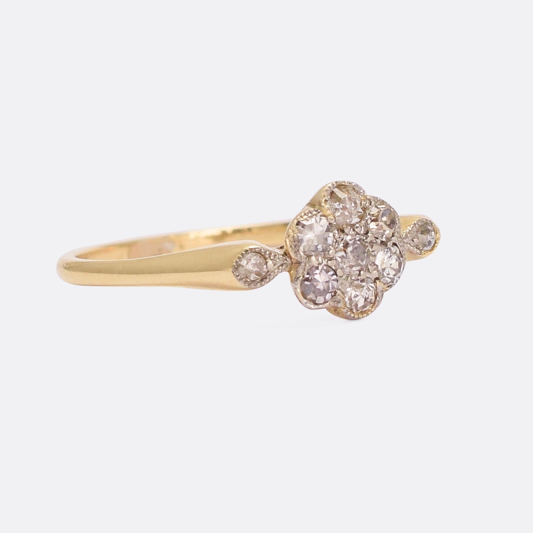 A lovely Edwardian diamond daisy ring modelled in 18 karat gold with millegrain platinum settings. It's set with eight-cut diamonds, seven to the head and a further two shoulder accents; the stones have big facets that produce bright flashes and