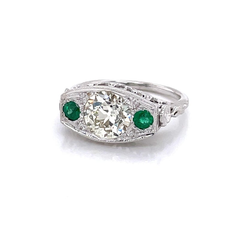 Gorgeous antique Edwardian eighteen karat 18K white gold ring with its regal oblong shape features a beautiful 1.60 carat round faceted Miner's Cut diamond highlighted by two faceted .06 carat natural green round faceted emerald gemstones. The