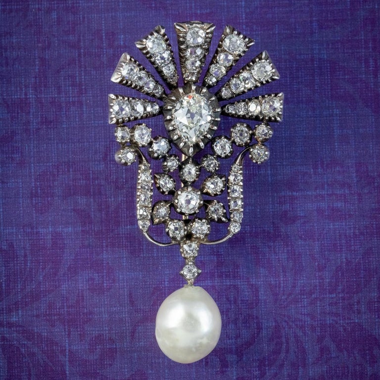 A stunning antique Edwardian brooch from the early 1900s decorated with a dazzling array of diamonds and a large pearl at the bottom, dotted with a hidden pearl underneath.  

The diamonds are a combination of old mine and cushion cut, with a