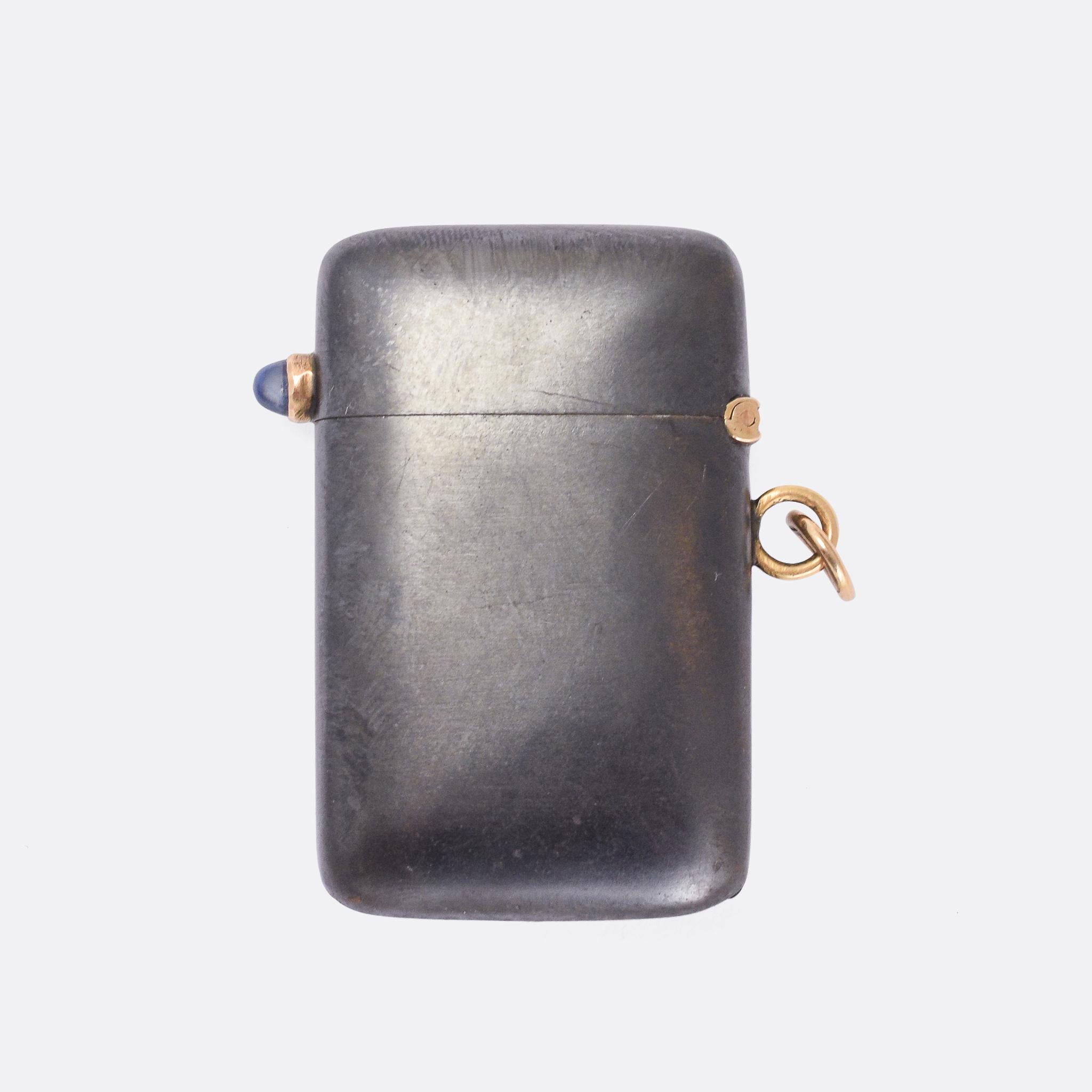 A cool antique vesta case dating from the early 20th Century. It's constructed in gunmetal, with 9 karat gold fittings (hinge, bail, etc), and set with an old cut diamond and a deep sapphire cabochon. The colour contrast between the gold and the
