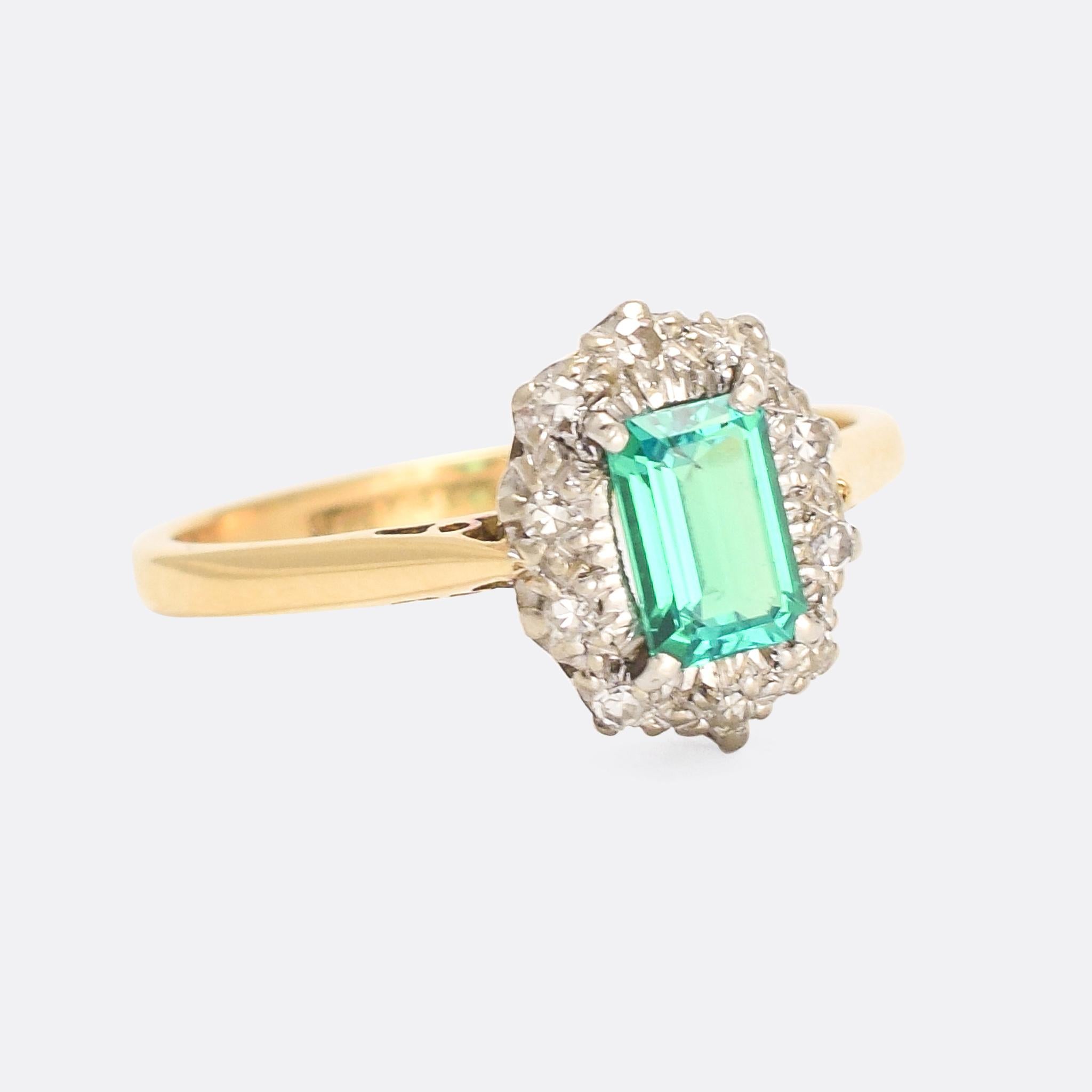 A stunning Edwardian emerald and diamond cluster ring dating from the early 20th Century, circa 1910. The principal stone is a vibrant (likely Colombian origin) elongated emerald cut emerald, perfectly accented with icy white diamonds and platinum