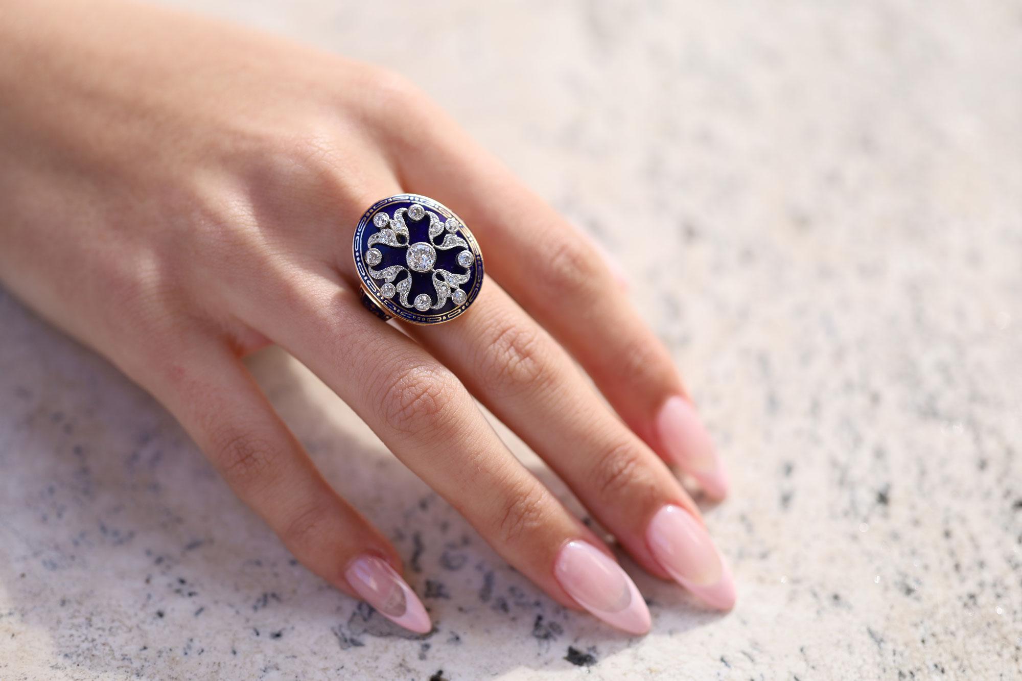 Appearing as if pulled from a treasure chest, this authentic, Edwardian antique cocktail ring is a coveted heirloom. The deep blue enamel background is adorned with a scrolling diamond shield of highly worked milgrained platinum along with an