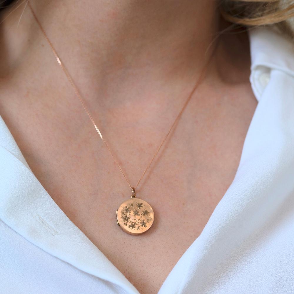This antique round locket is crafted in warm rose gold and richly engraved on both sides with intricate floral motifs. The front features a delicate trailing flower design, while the reverse displays a floral wreath framing the stamped hallmark. The