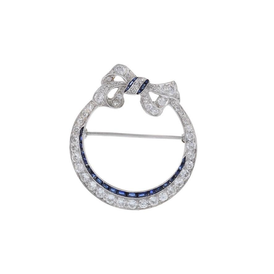 Step into the elegance of the Antique Edwardian Era with our Platinum Sapphire and Diamond Circle Bow Lapel Pin. This exquisite piece combines the sophistication of platinum with the allure of sapphires and diamonds. The circular bow design adds a