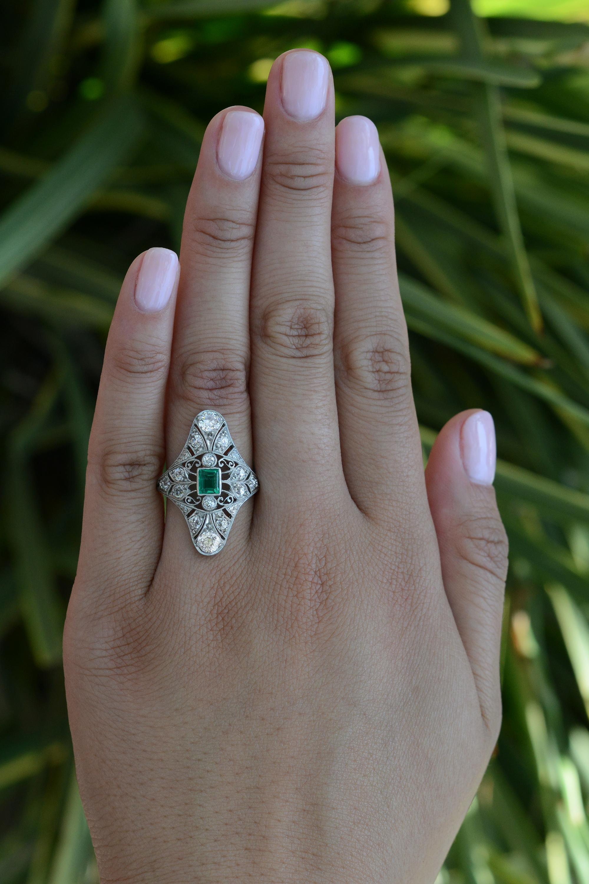 This exquisite emerald and diamond navette dinner ring is an authentic Edwardian statement piece that is sure to become a treasured heirloom. Centering on a vivid, lush medium grass-green emerald with 14 old European and old mine cut diamonds