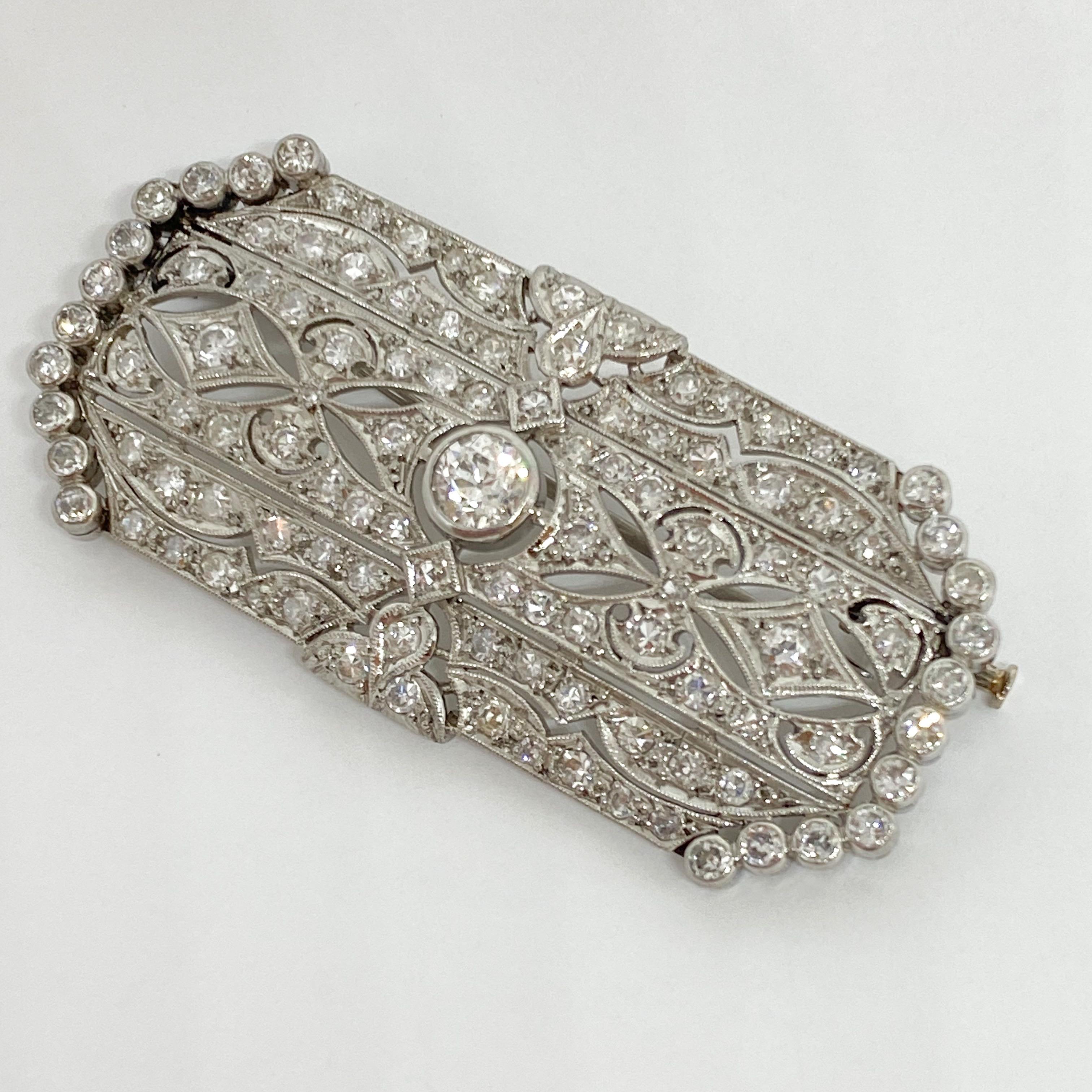 Lovely Edwardian filigree cutout wide brooch designed in Platinum. The main diamond is Old European Cut and weighs approximately 0.57 carats. The rectangular brooch is covered in pave set diamonds. Hinged brooch pin and plunger on the back. The