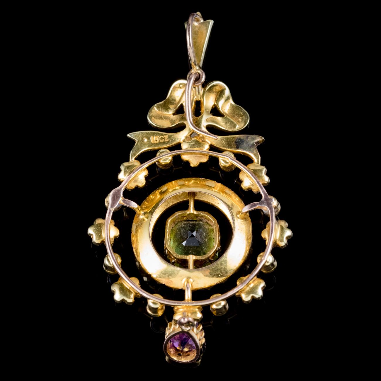 A pretty antique Edwardian Suffragette pendant modelled in 15ct Yellow Gold with a border of flowers and a bow crowned on top. Decorated with lovely lustrous Pearls, a teardrop Amethyst dropper and a square cut Peridot in the centre. Suffragette