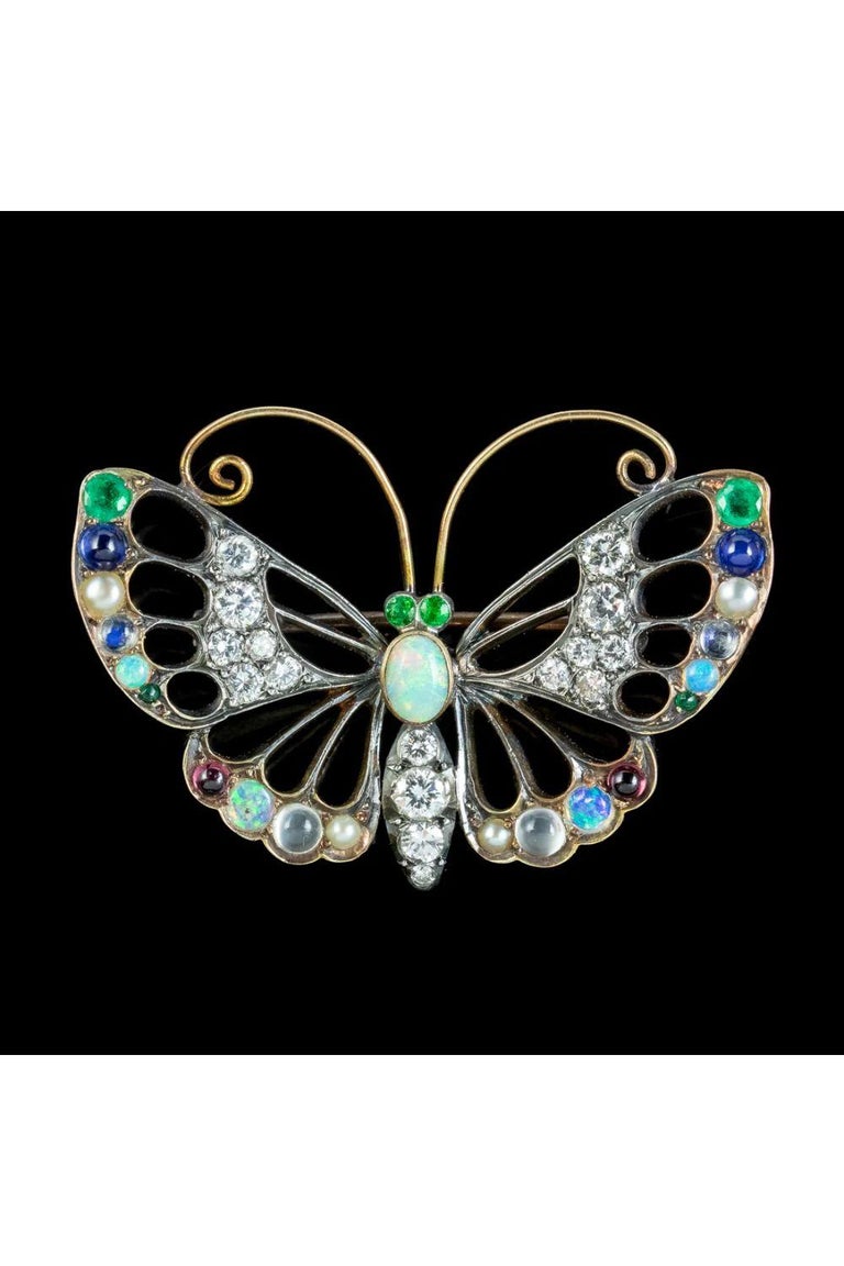 A colourful antique Edwardian butterfly brooch decorated with a glittering rainbow of gemstones. A natural cabochon opal sits at the head of the butterfly along with green peridot eyes. Brilliant cut diamonds are encrusted across the abdomen and the