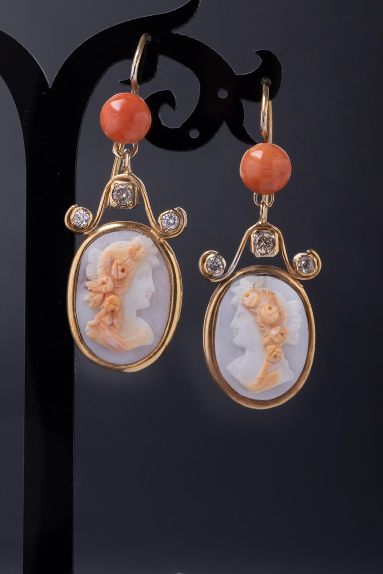 A classy pair of early-1900's antique cameo earrings. 

The earrings have a classic long solid gold body decorated with stunning oval cameos, diamonds and coral. The cameos are hard stone and depict young ladies with curly blond hair. Hard stone