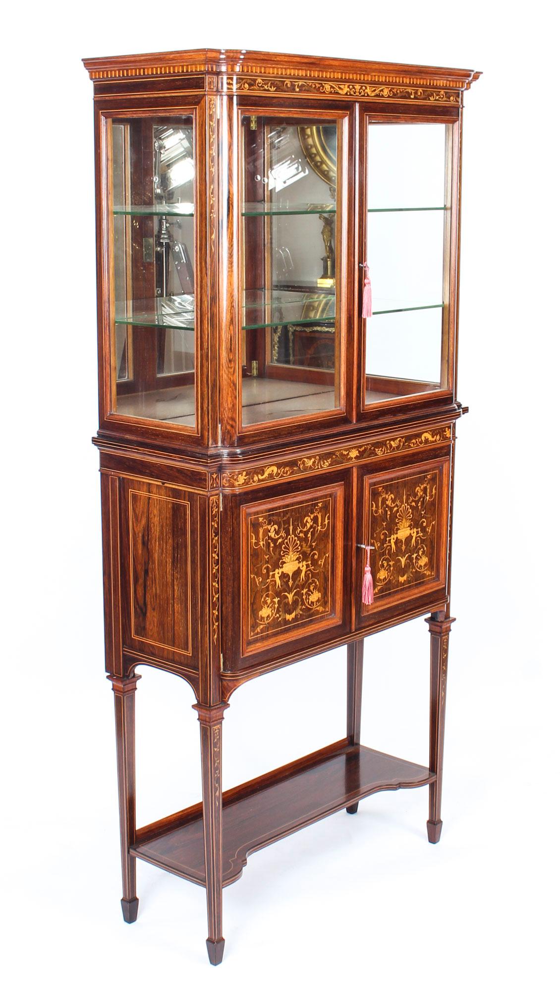 This is a truly magnificent antique Edwardian Goncalo Alves and marquetry inlaid upright display cabinet by Edwards & Roberts, circa 1890 in date.

The cabinet is bordered with boxwood lines and decorated with scrolling foliage, cherubs, mythical