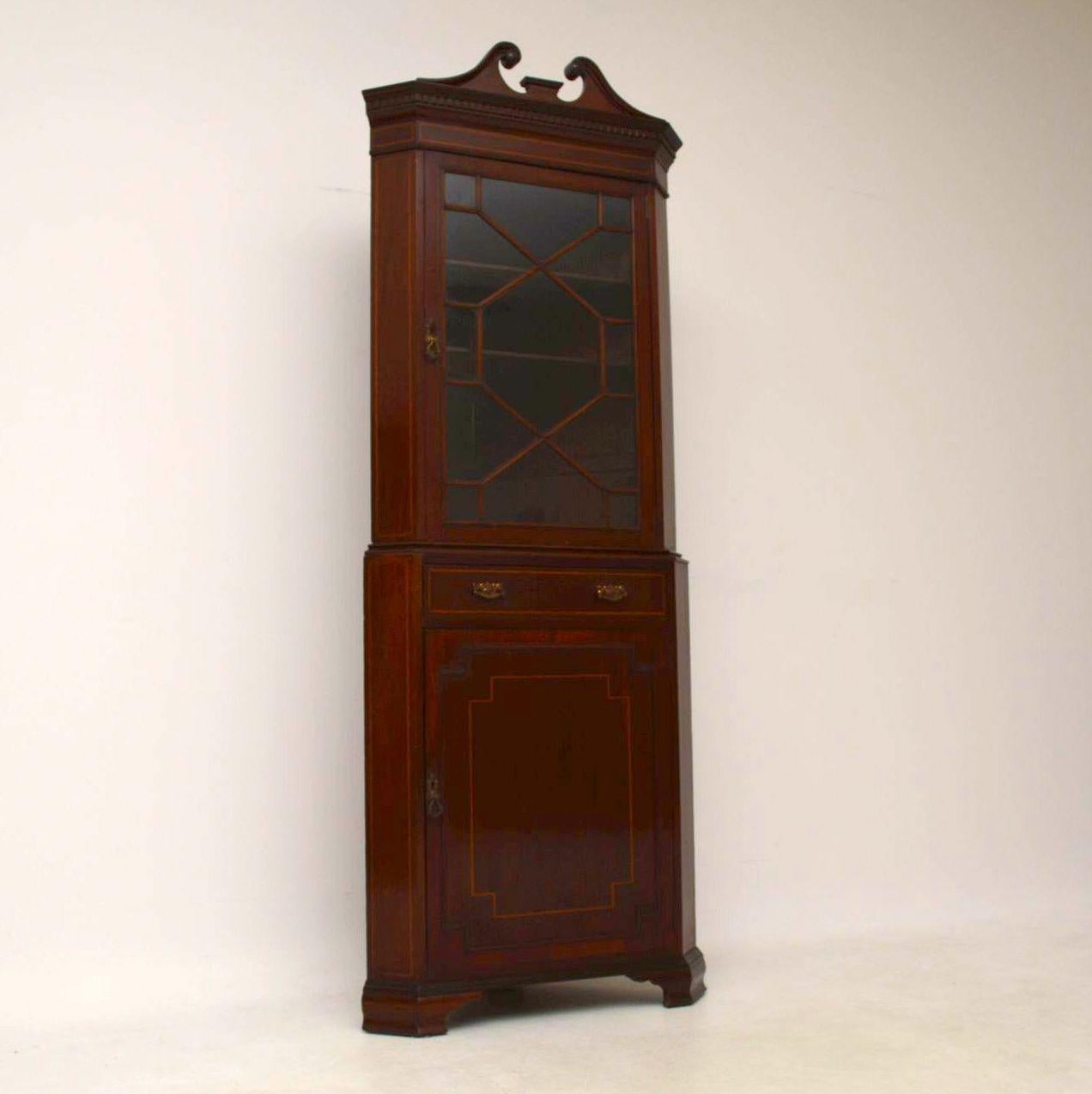Antique Edwardian inlaid mahogany corner cabinet with an astral-glazed top section and cupboard below. It’s in good original condition and comes apart into two sections for easy transportation. There is a swan neck pediment on the top with a dental