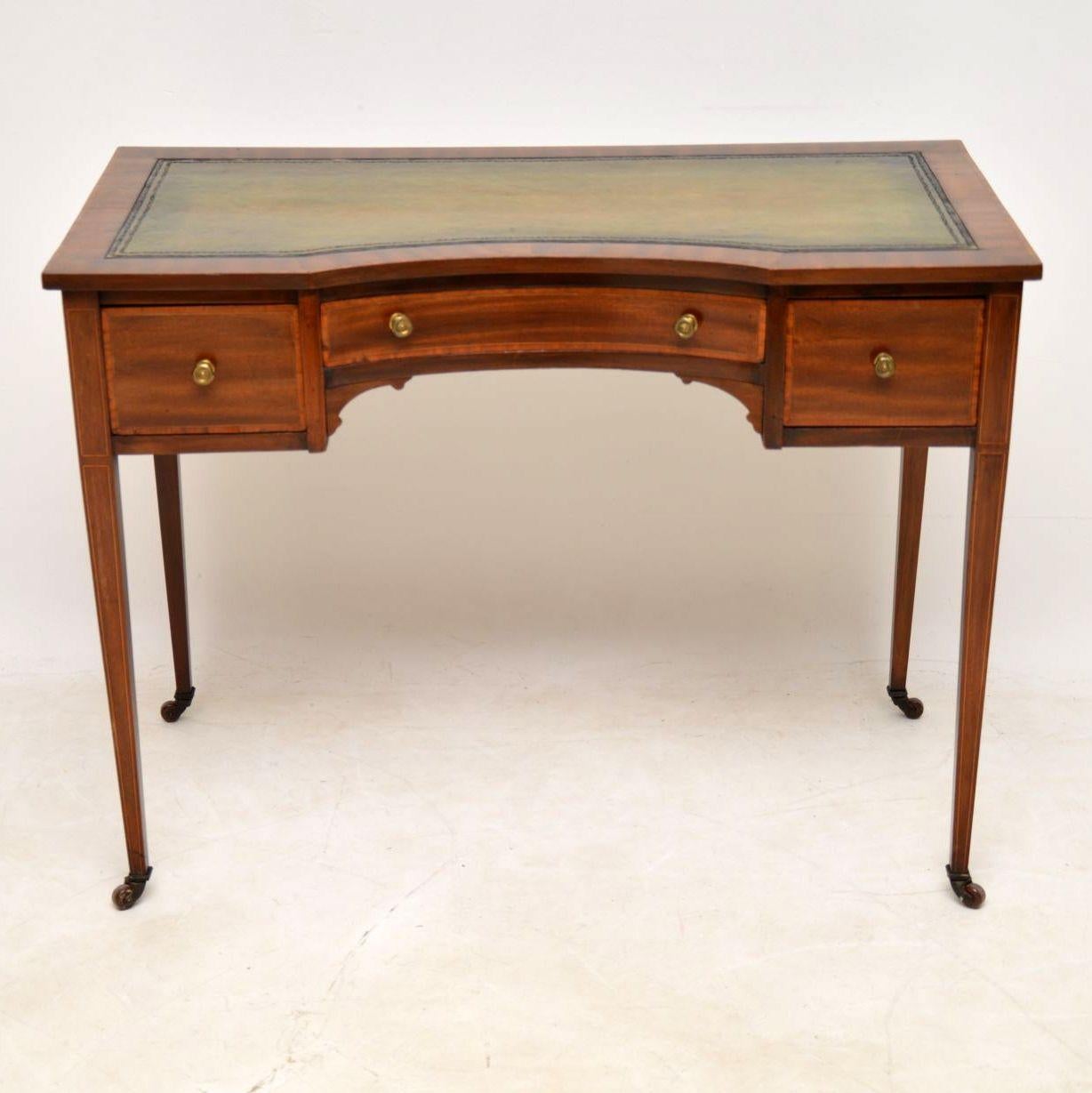 Elegant antique Edwardian mahogany desk with a tooled leather writing surface and some fine satin wood inlays. It has a concave front, three drawers with fine dovetails, original brass handles and porcelain casters. This desk dates from the