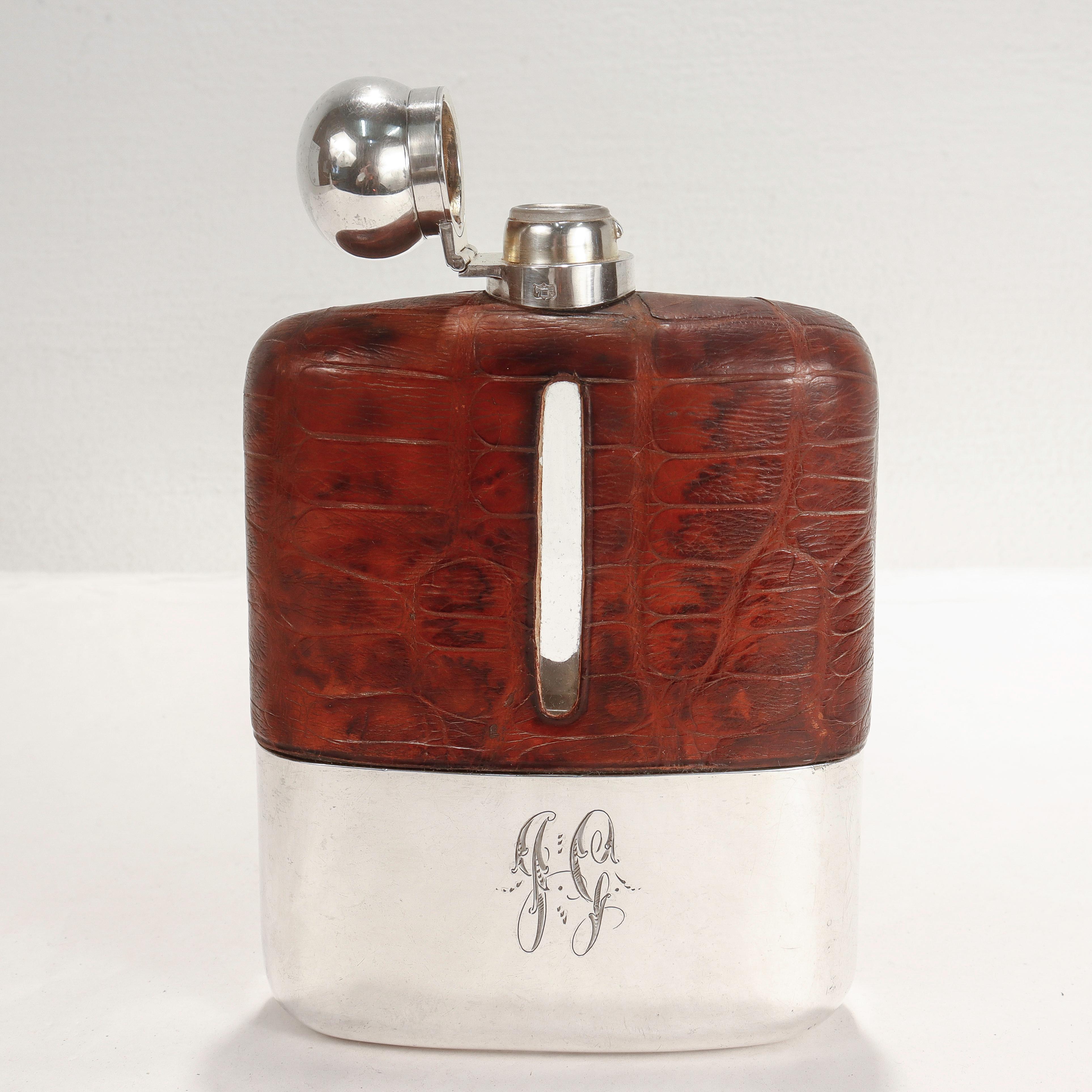 A smart Edwardian liquor or whiskey hip flask.

By James Dixon & Son. 

In silver plate, glass, and leather. 

With a removable silver plate cup to the base, twist top stopper to the top, and an embossed 'alligator' pattern leather cover to