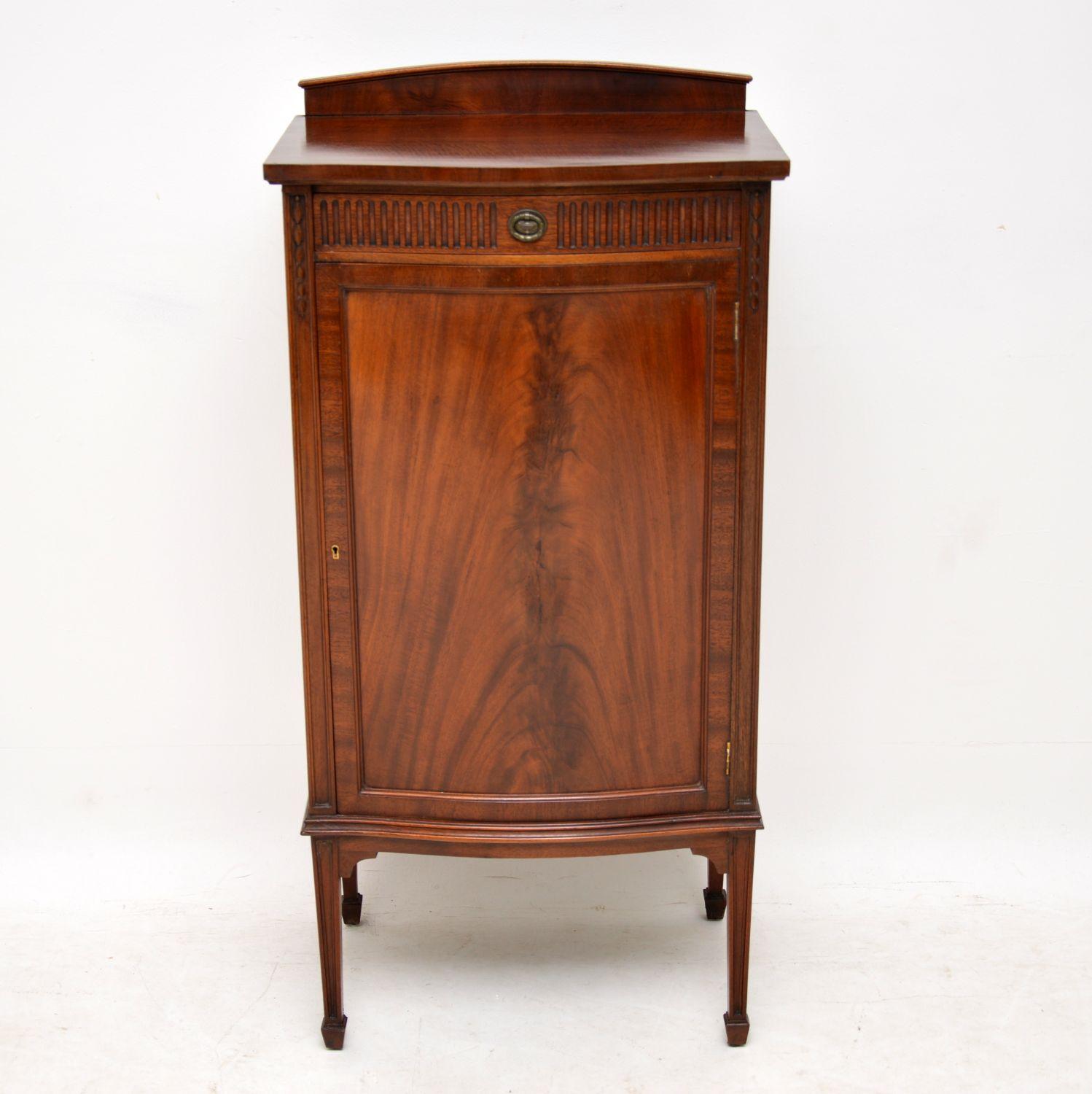 Antique Edwardian mahogany bow fronted cabinet with a flame mahogany panelled door & sitting on tapered spade end legs. It’s fine quality, in good condition and dates to circa 1890-1910 period. There’s a back gallery on the top and the top surface