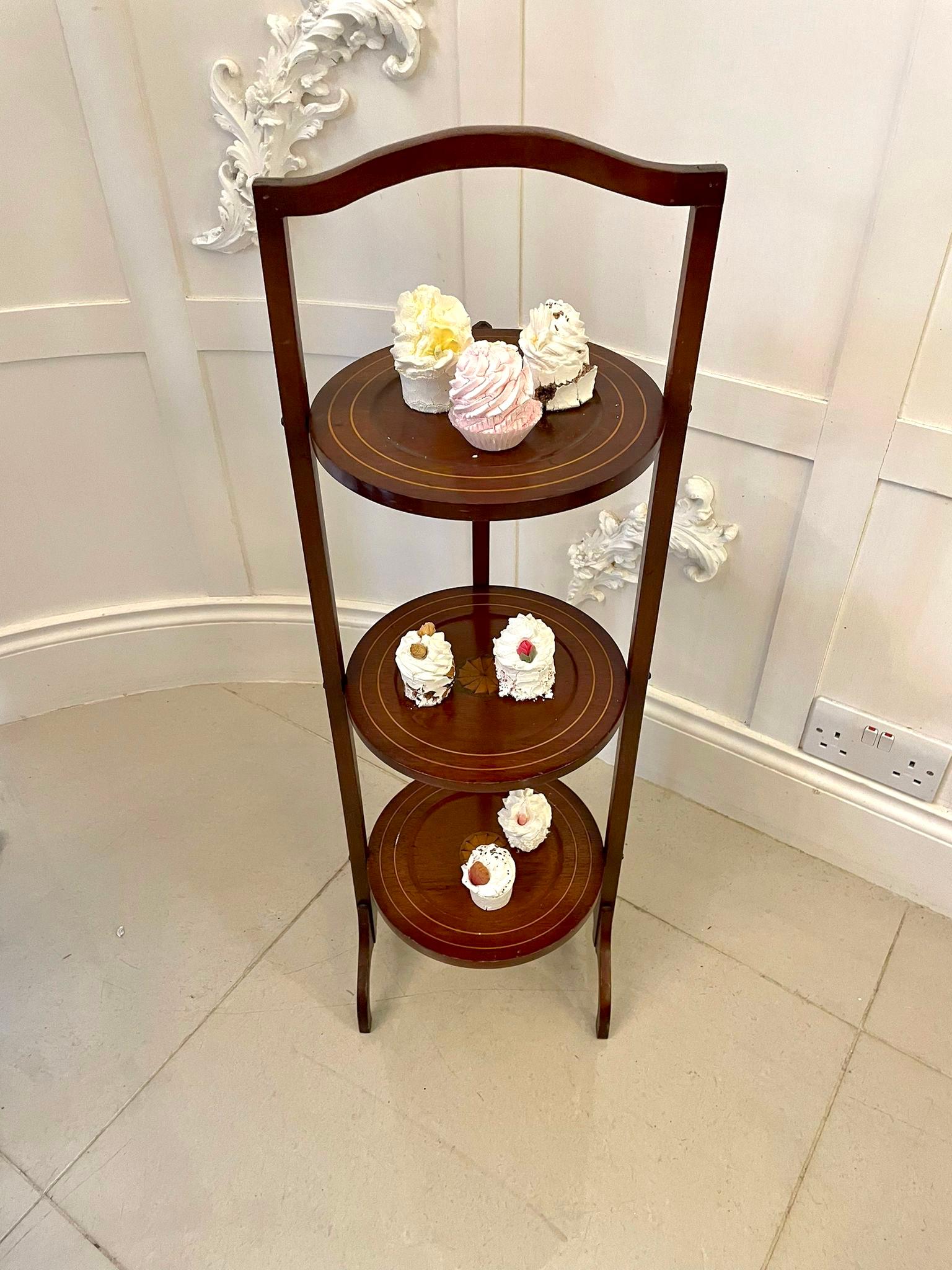 Antique Edwardian mahogany inlaid folding cake stand having three folding circular tiers with satinwood stringing and inlaid satinwood shells, mahogany uprights with shaped handle and feet. 

Measures: 89 x 27 x 25.5 cm
Date 1900.
 