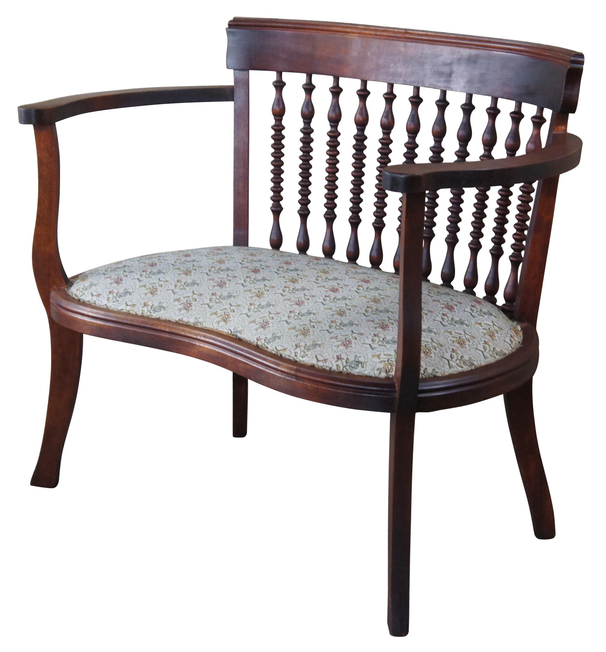 A lovely early 1900s Edwardian kidney shaped settee. Made from mahogany with a barrel back, turned spindles and a floral upholstered seat. Its quaint size makes it perfect for a parlor, library or sun room.