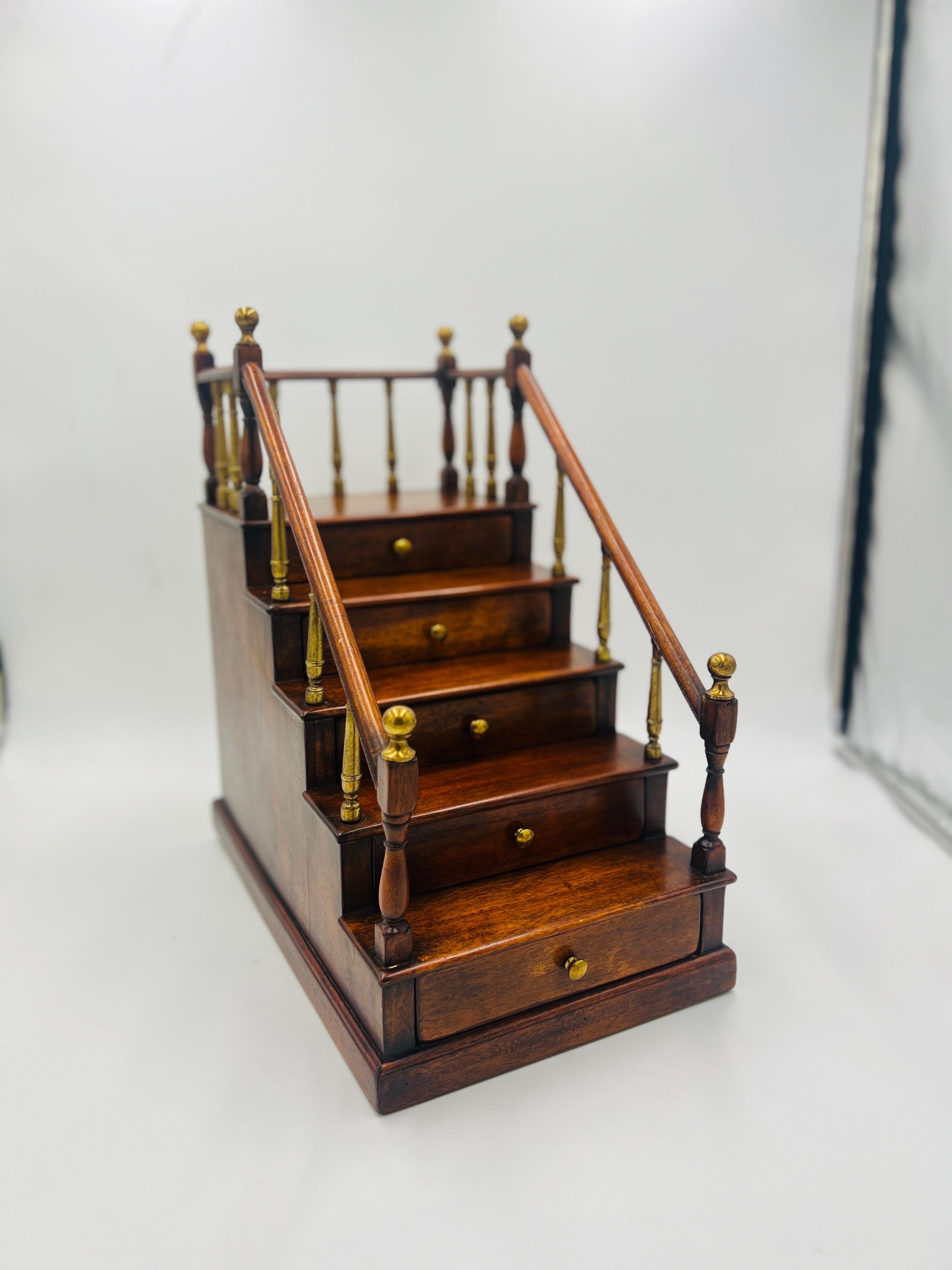 Antique English cabinet made mahogany staircase model. The model features a 5 step design with railing across the sides. Each railing accented by a brass finial. The 5 drawers each slide easily and have brass pulls. No apparent makers mark.