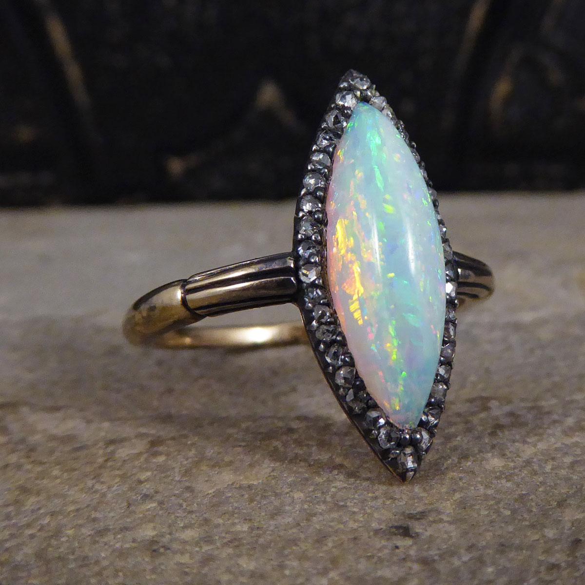 An exquisite and unusual ring for the Edwardian era. This wonderful ring features a lustrous Opal in the centre cut in a marquise shape with great colours reflecting from all angles, showing many greens, blues, oranges and reds. The Opal is