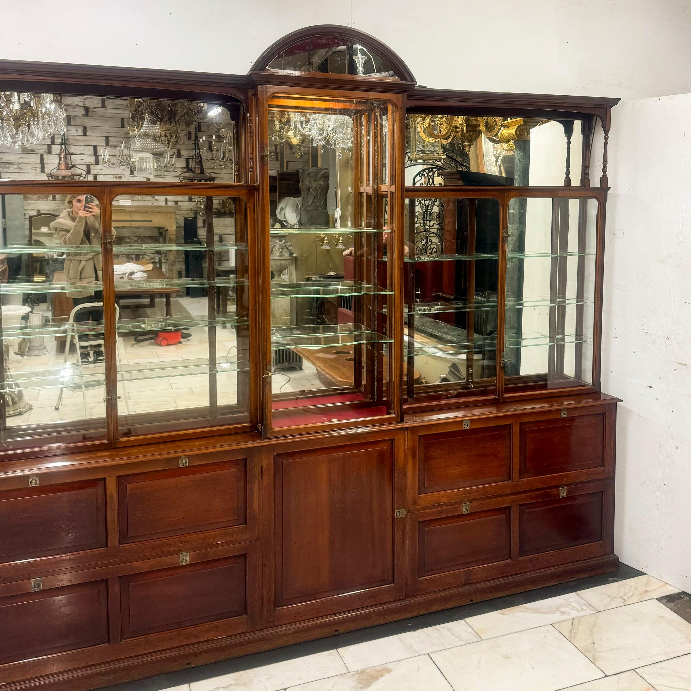 Esta exquisita vitrina de caoba eduardiana, fabricada en 1902 para una joyería de Devon, presenta un impresionante fondo de espejo y elegantes estantes de cristal, perfectos para destacar objetos finos. La base incluye cinco prácticos armarios con