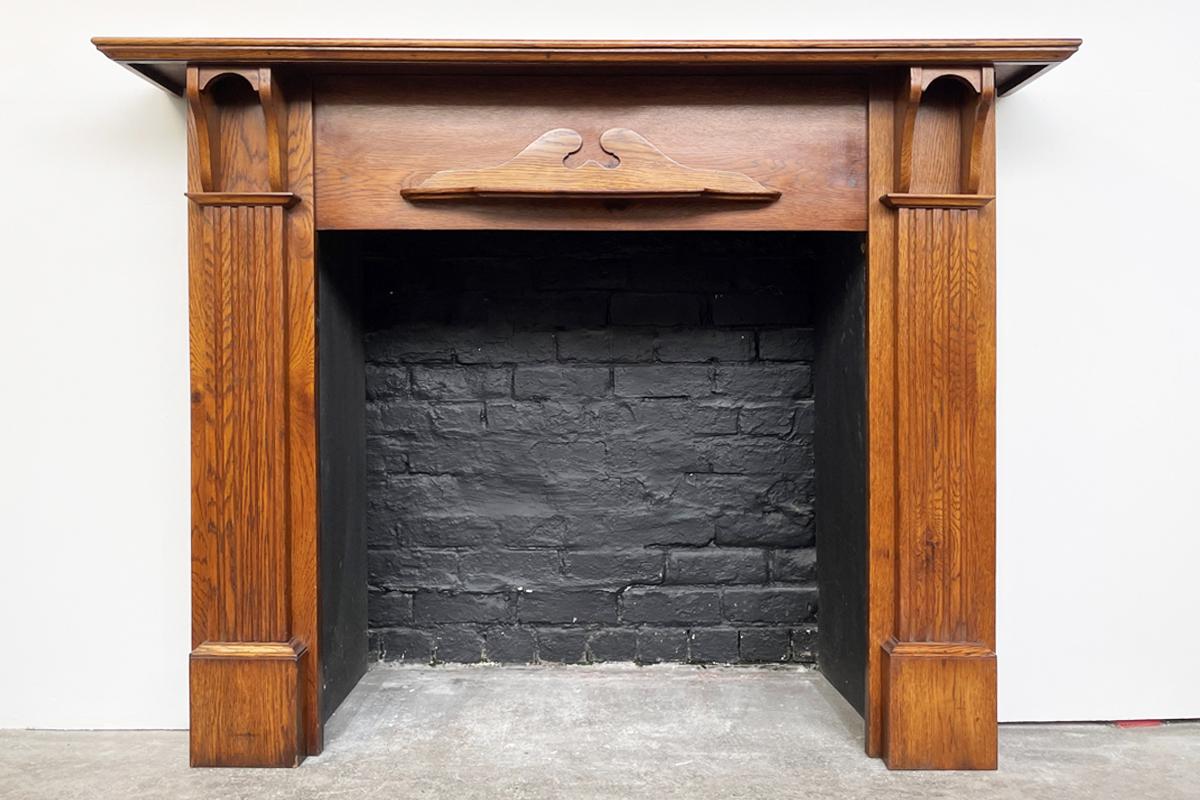 Antique Edwardian oak fire surround. The fluted legs terminate with bracket capitals supporting the generously deep shelf. A small secondary shelf can be found on the frieze. In great condition and colour with few but expected signs of wear and use.