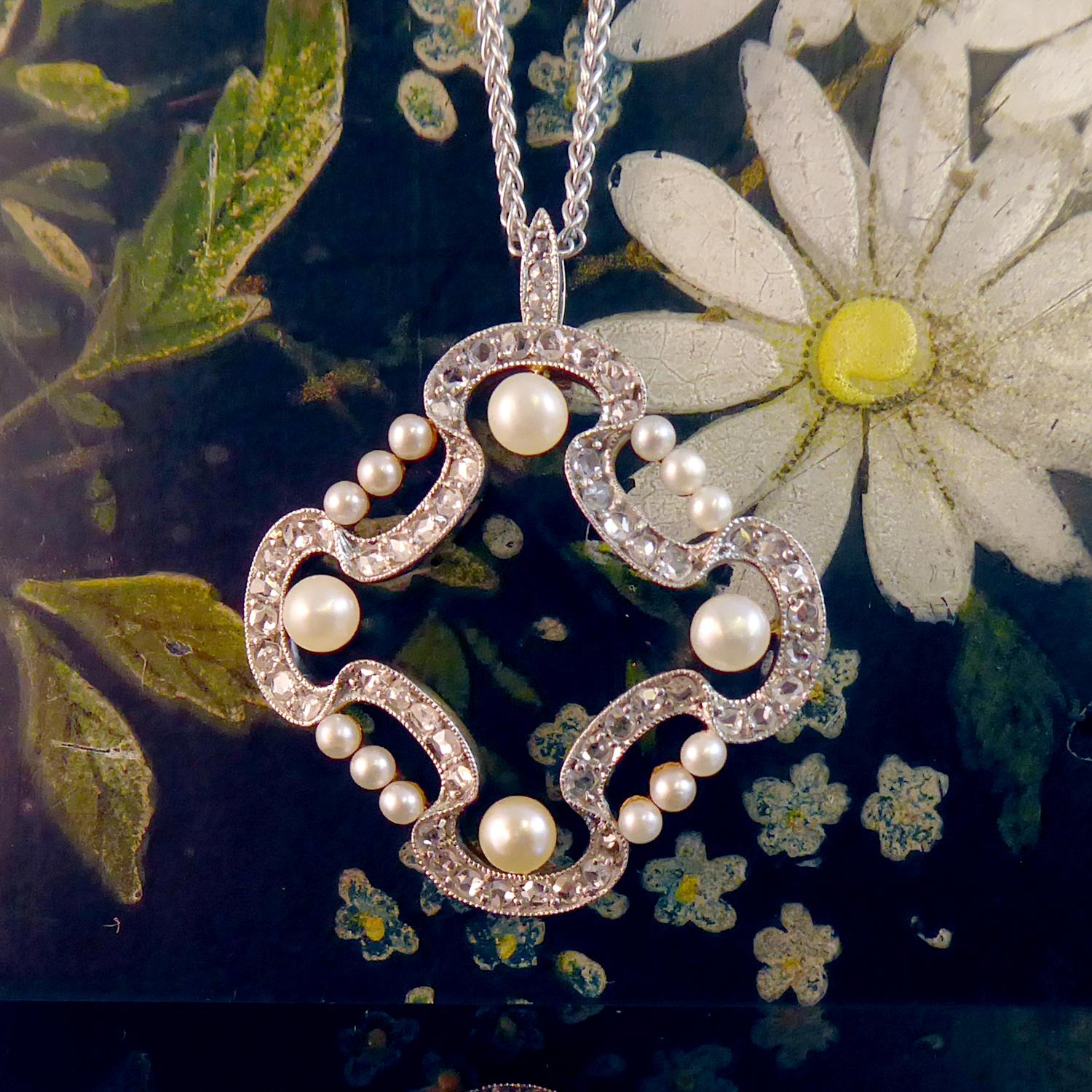 An antique Edwardian pendant of some 52 rose cut diamonds, approx. 1.0mm to 1.2mm, bead set into a milled grain edge ribbon garland.  Four white/cream round pearls, each approx. 3.5mm diameter, are set to the top. bottom, left and right of the