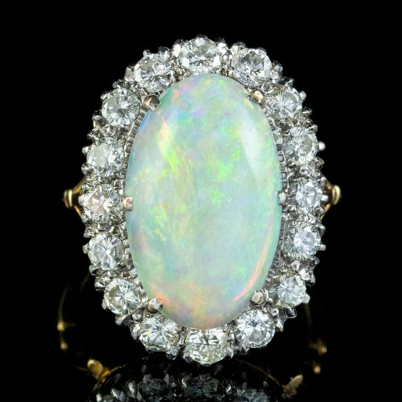 Une spectaculaire bague à grappe Edouardienne ancienne exposant une opale naturelle cabochon envoûtante, encadrée par seize diamants étincelants de taille brillant, totalisant environ 1,6ct. L'opale présente un kaléidoscope de couleurs vives et pèse