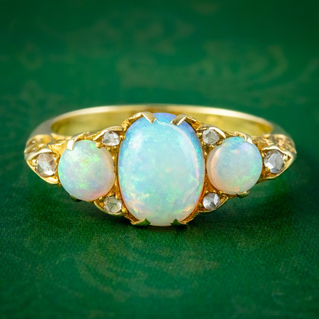 A glorious antique Edwardian carved half hoop ring adorned with a trilogy of natural opal cabochons displaying a kaleidoscope of vibrant colours that dance across the surface. They weigh approx. 1.7ct in the centre and 0.40ct on either side with six