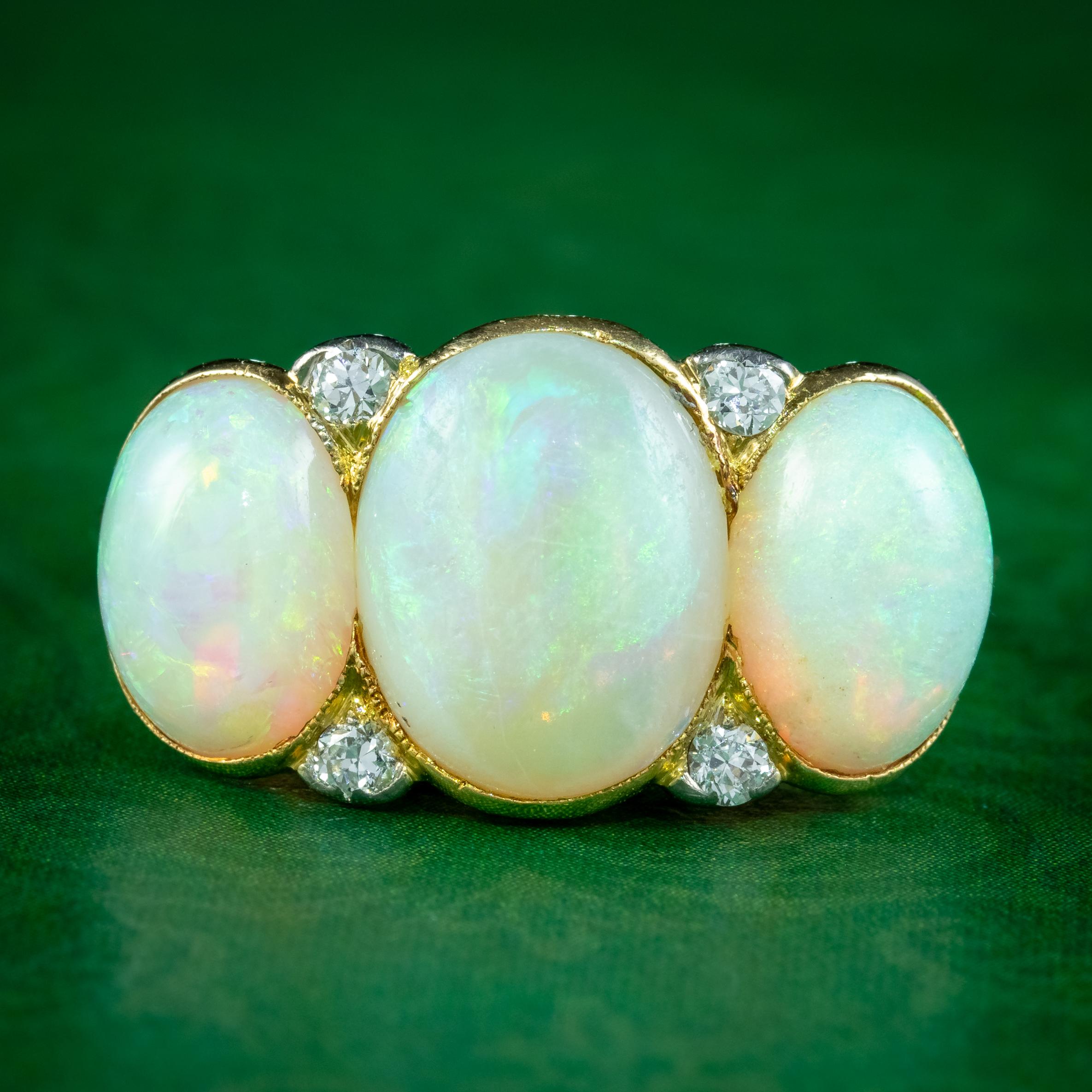 A magnificent antique Edwardian ring adorned with a trilogy of natural opal cabochons displaying a kaleidoscope of vibrant colours that dance across the surface. They weigh approx. 3.5ct in the centre and 1.75ct on either side with four twinkling