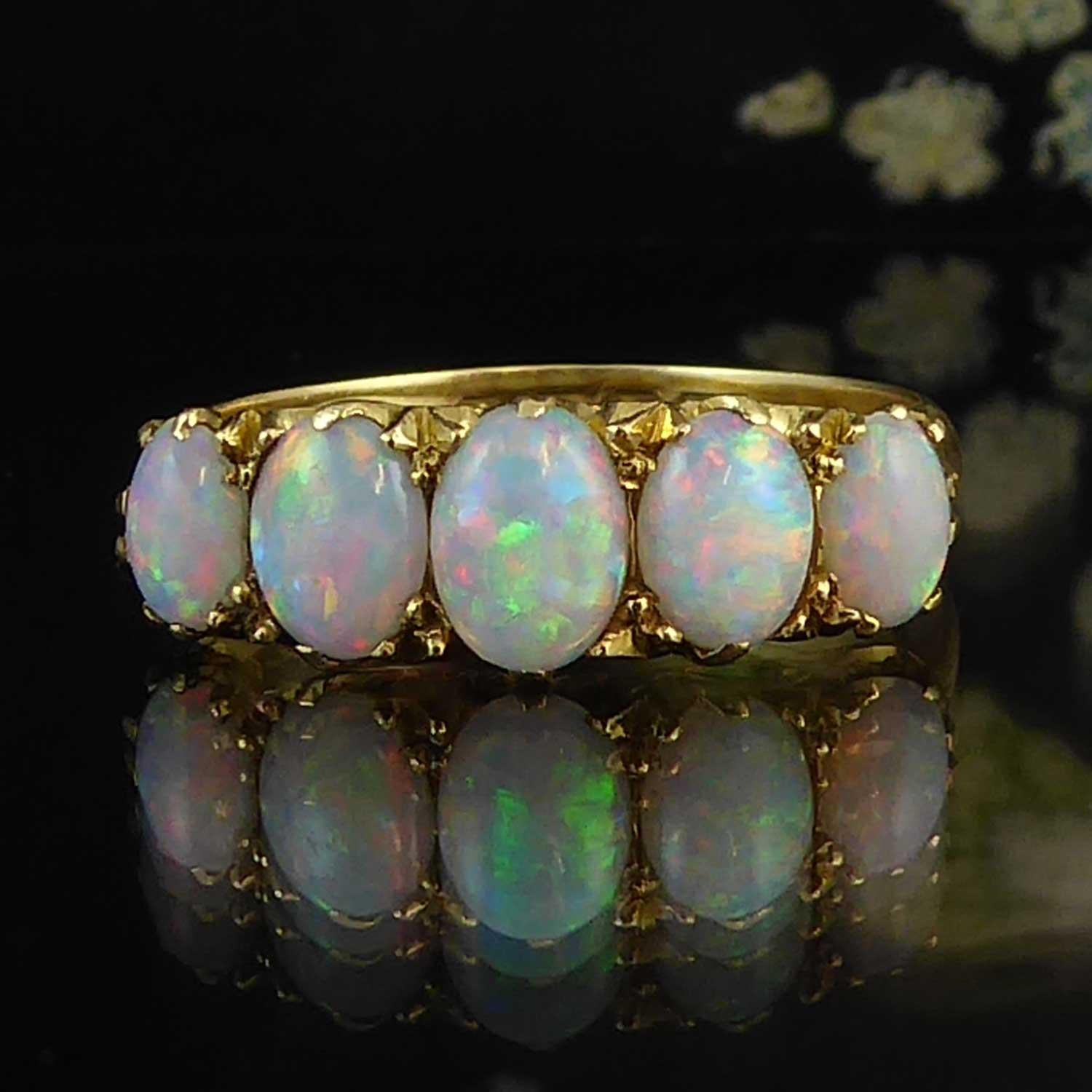 An antique opal ring set with five cabochon cut oval opals graduating in size from the centre opal at approx. 3.0mm x 5.0mm to 2.0mm x 4.0mm at each end. Displaying a play of blue, green and orange fire, the opals are complimented by the yellow gold