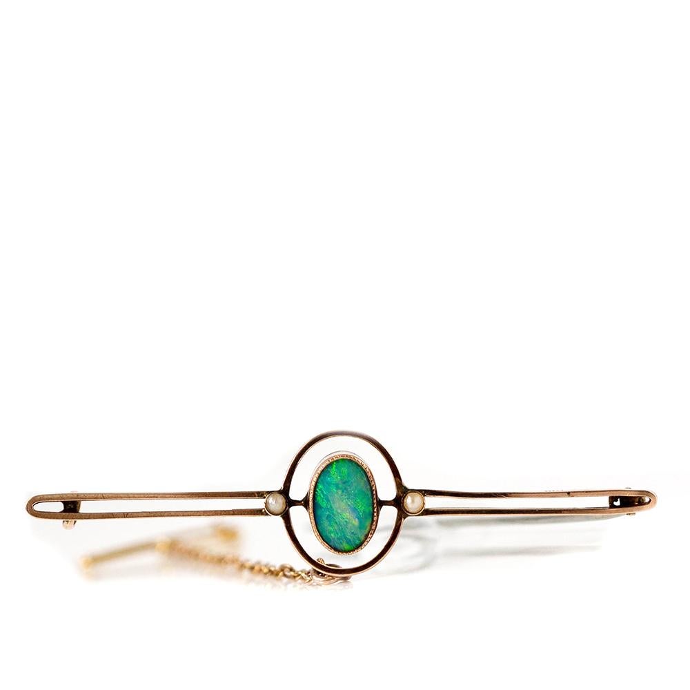 Discover our exquisite doublet opal and seed pearl brooch. The central gemstone features a beautiful opal, radiating green-blue hues set in 9ct yellow gold. Complementing this opalescent wonder, two tiny seed pearls are nestled on either side. Set