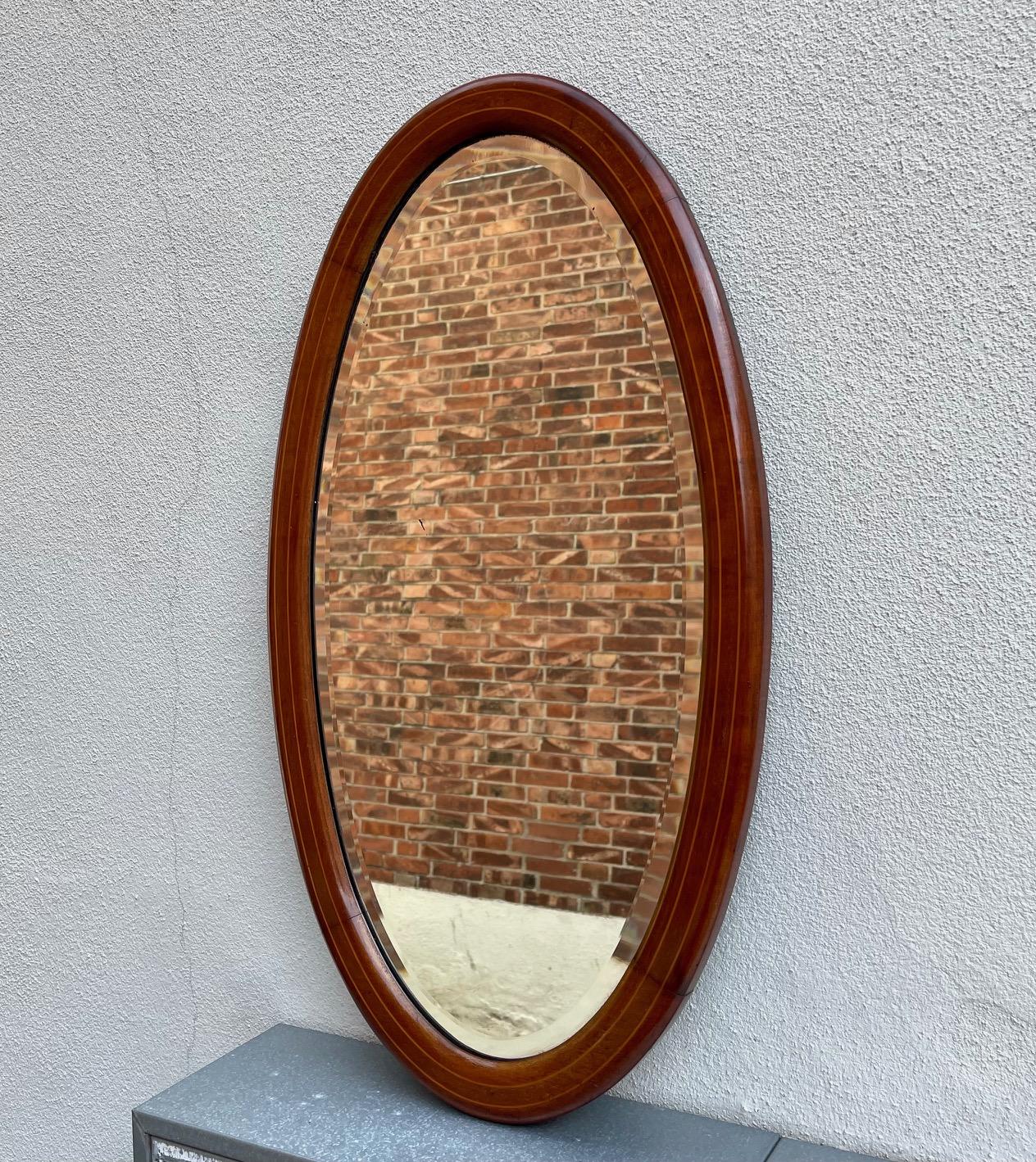 Small Oval Edwardian wall mirror. Executed in solid walnut inlaid with cherry. Beveled mirror glass. Made by an anonymous cabinetmaker in Denmark or England circa 1910. Measurements: 67x37 cm (26x14 inch).