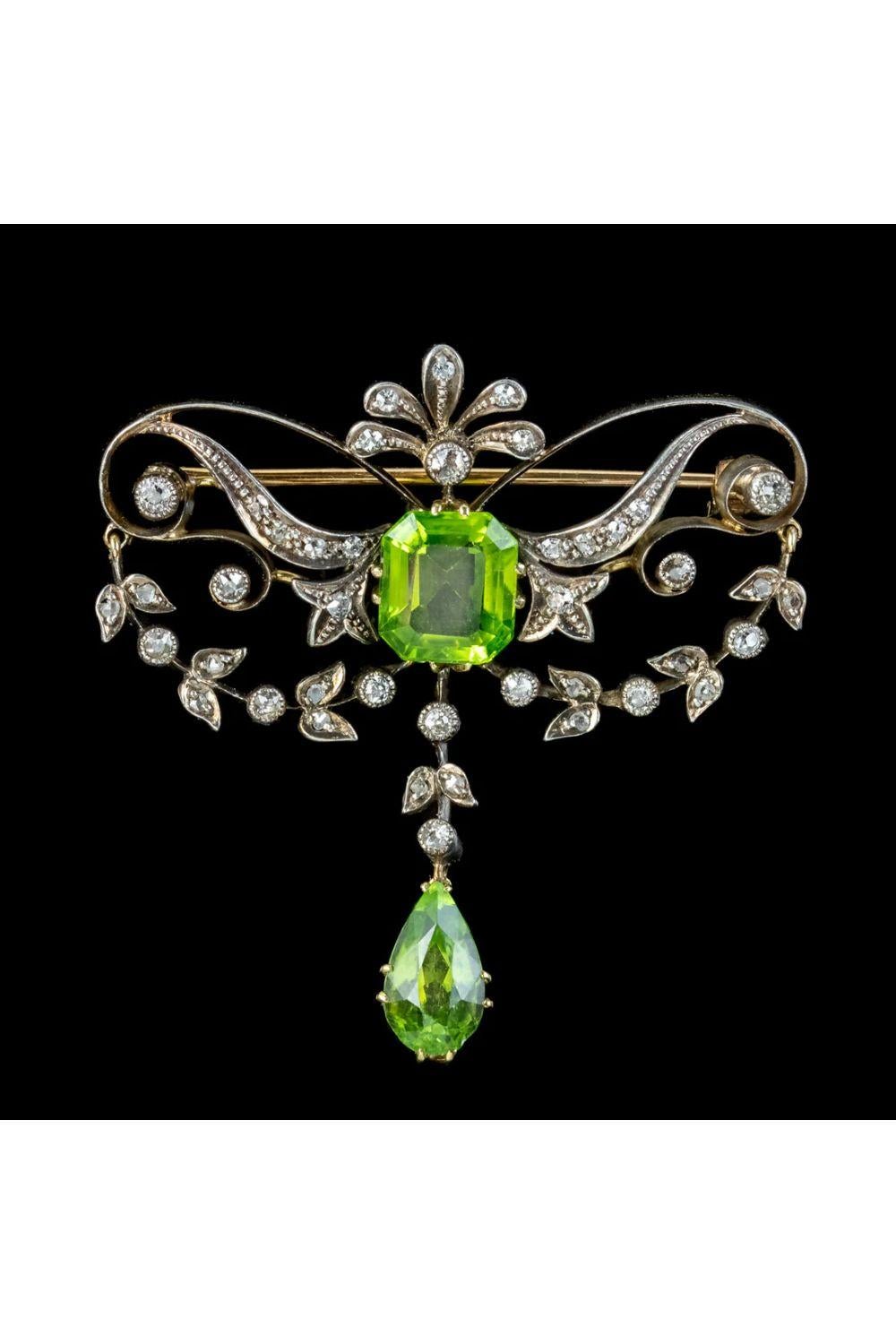 A beautiful antique Edwardian brooch made in the Art Nouveau style with flowing curves and foliate garlands decorated with twinkling diamonds (approx. 1ct total) and two rich green peridots (approx. 5.5ct total). 

The largest peridot is a gorgeous