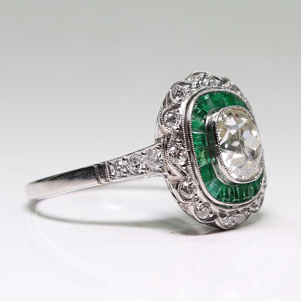 Period: Edwardian (1901-1920)
Composition: Platinum.

Stones: 
•	1 cushion Old mine cut diamond of J-VS2 quality that weighs 1.34ctw. 
•	14 Old mine cut diamonds of H-VS2 quality that weigh 0.40ctw. 
•	19 Natural calibrated cut emeralds that weigh