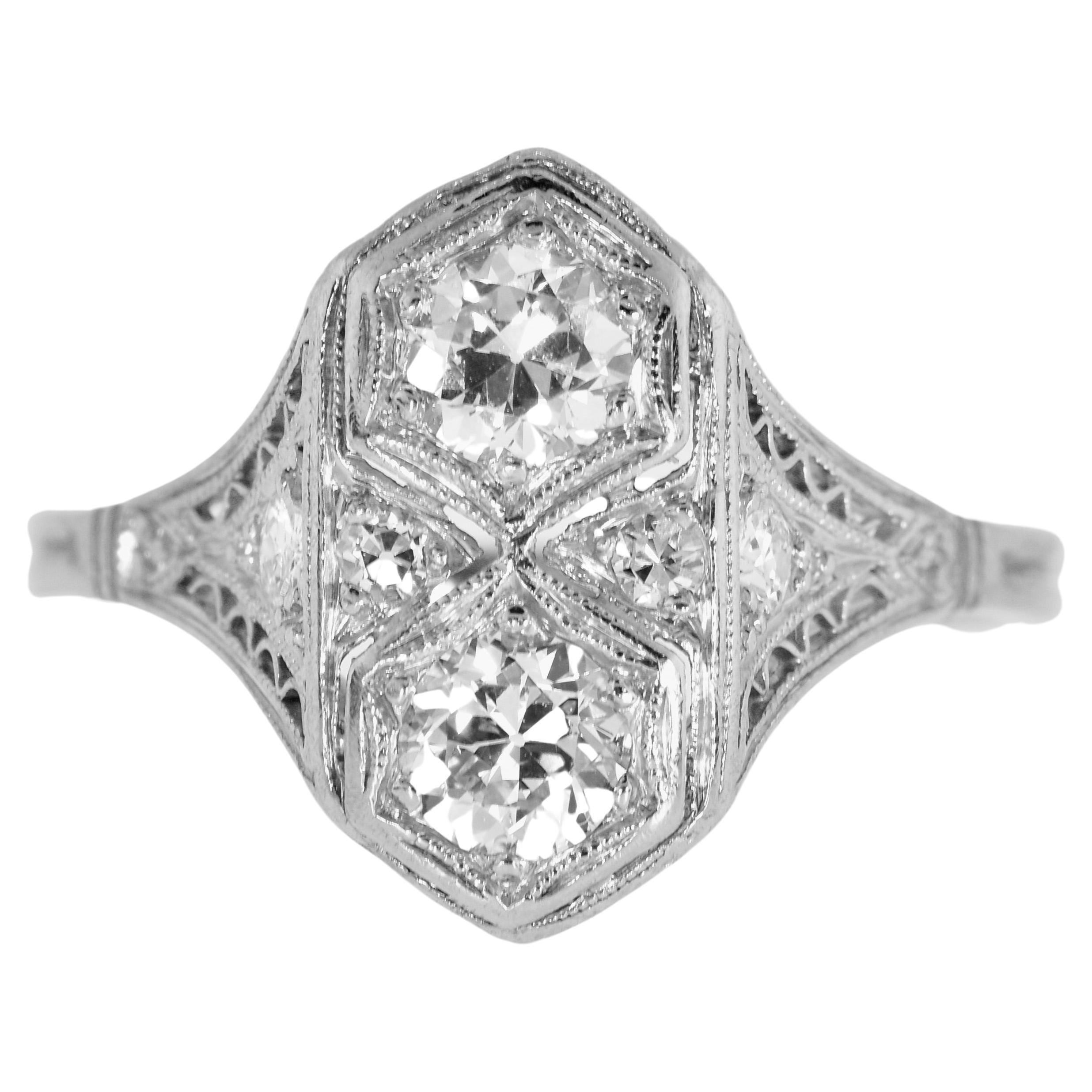 Antique Edwardian platinum and diamond ring, circa 1915.  In fine condition this filigree platinum ring centers two European cut diamonds.  The well matched stones are near colorless (H), and VS, very slightly included.  Accenting and set on either