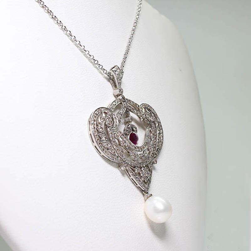 Period: 
Composition: Platinum.

Stones:
•	180 Old mine cut diamonds of K-VS2/SI1 quality that weigh 2.80ctw. 
•	1 Round cut natural ruby that weighs 1ctw.
•	1 Culture pearl of 10mm.
Measures: 65mm by 42mm 
Thick: 10mm
Total weight: 13.3grams –