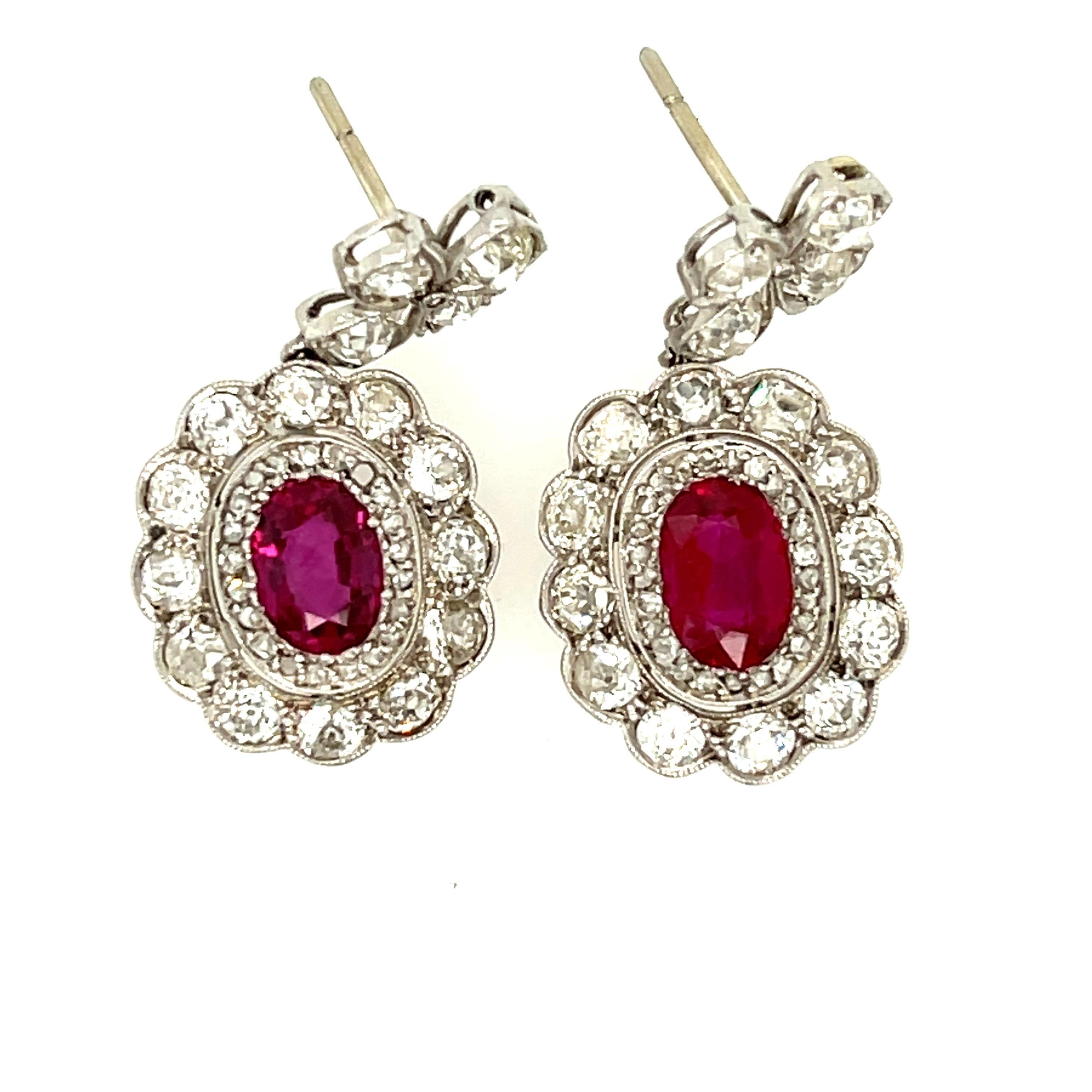 A pair of antique Edwardian platinum and diamond Burma ruby earrings, circa 1910. These lovely earrings feature a cluster of diamonds surrounding oval rubies hanging from a diamond floral motif top. The oval rubies are a rich red, weighing