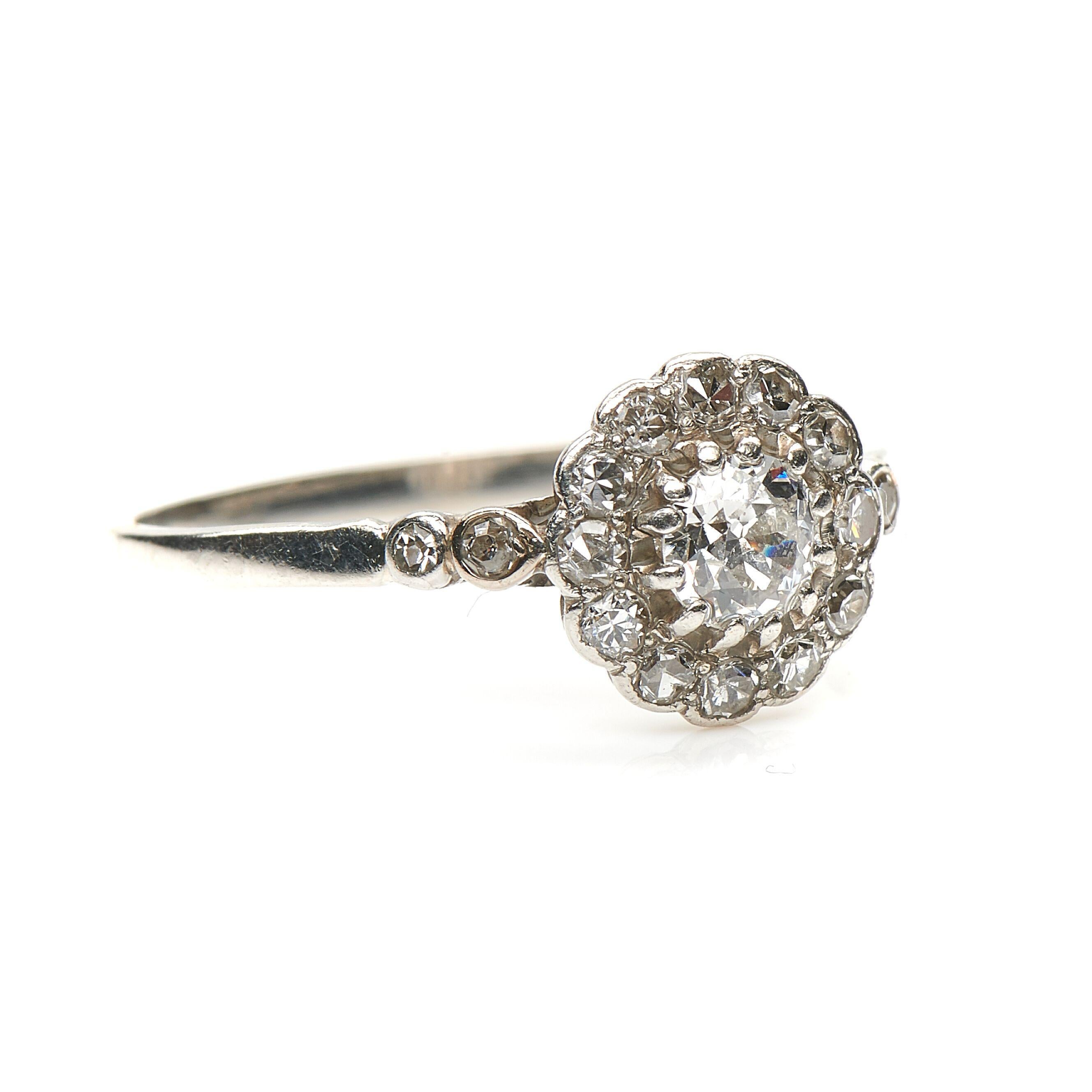 Antique, diamond engagement ring, circa 1910. Set to centre a round old cut diamond in a open-backed claw setting framed by a boarder of delicate smaller diamonds all rubover set in platinum. Further diamonds descend the shoulders to enhance the